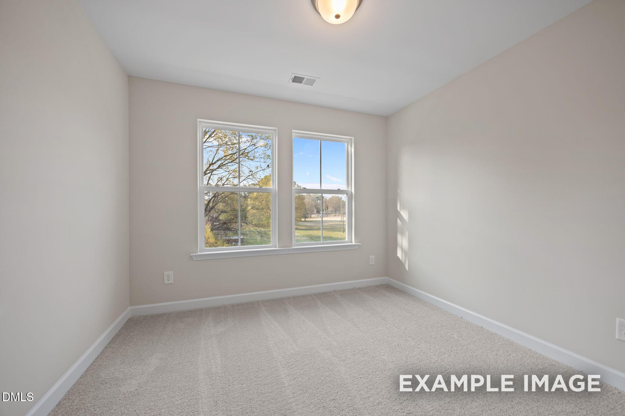Bright secondary bedroom with neutral walls, plush carpet, and large windows overlooking trees in Davidson Homes The Avery, Knightdale, NC