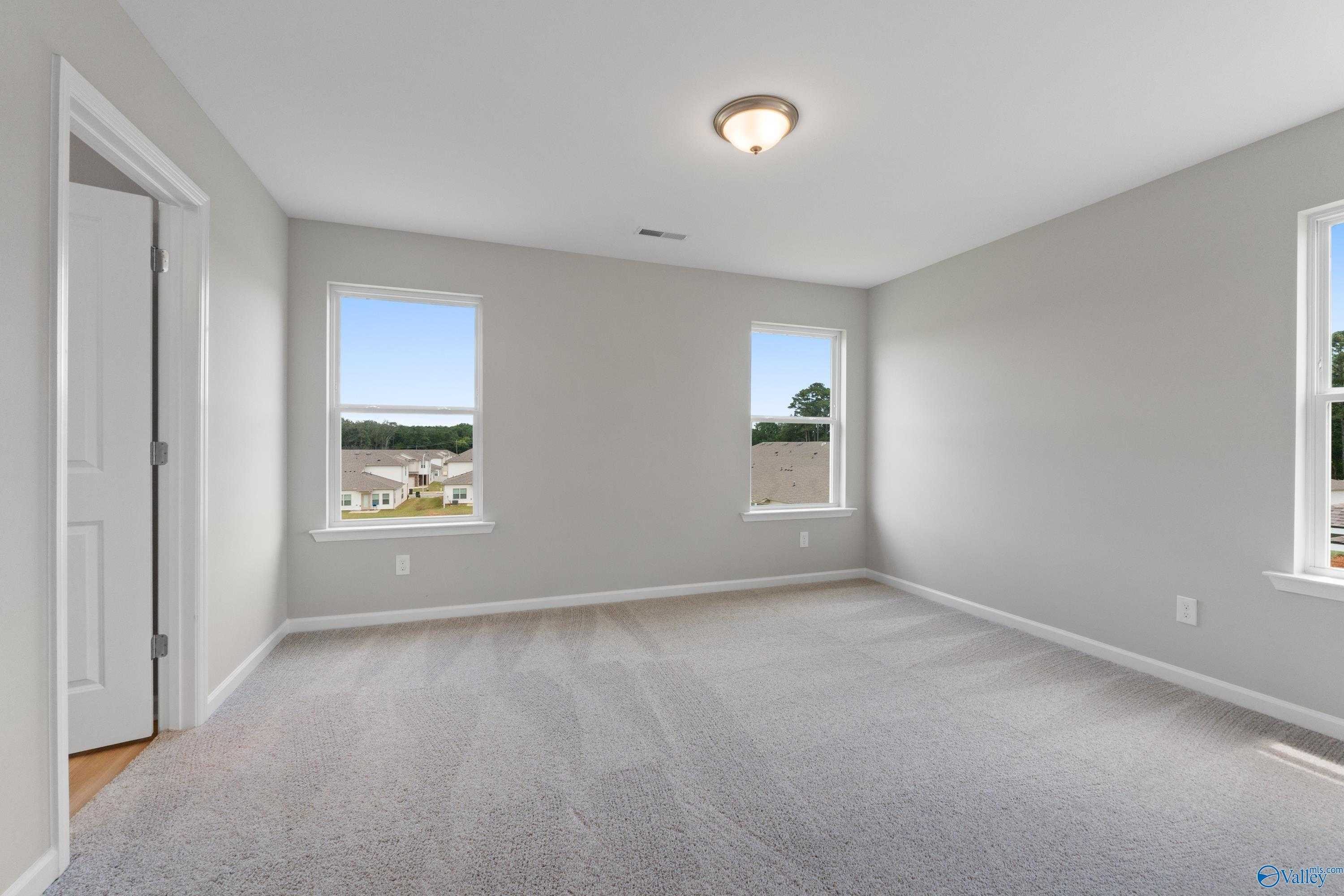 Bright secondary bedroom with gray walls, beige carpet, and large windows in Evermore Homes The Augusta, Madison Alabama