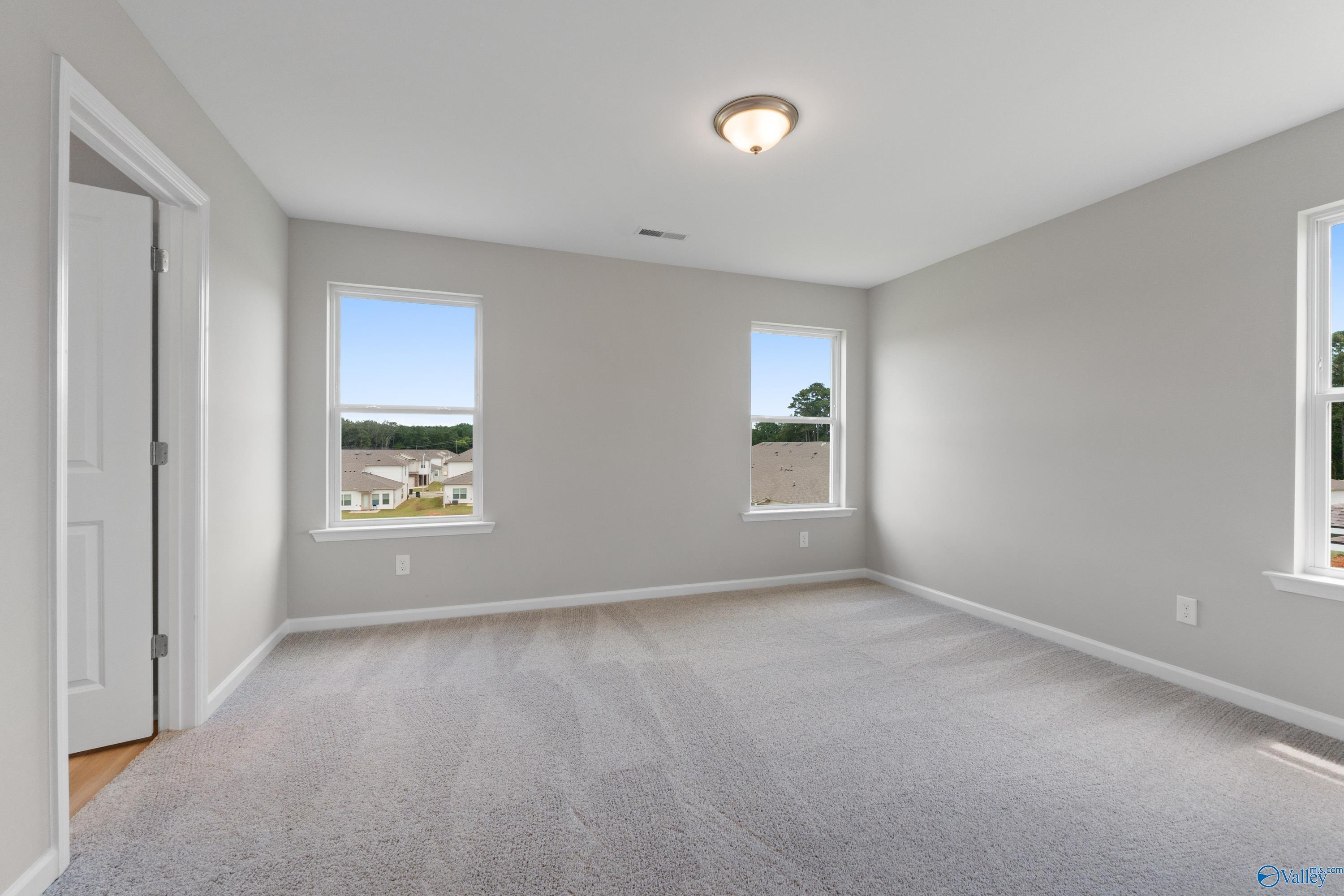 Bright secondary bedroom with gray walls, carpet flooring, and large windows overlooking neighborhood in Davidson Homes The Augusta, Madison, Alabama