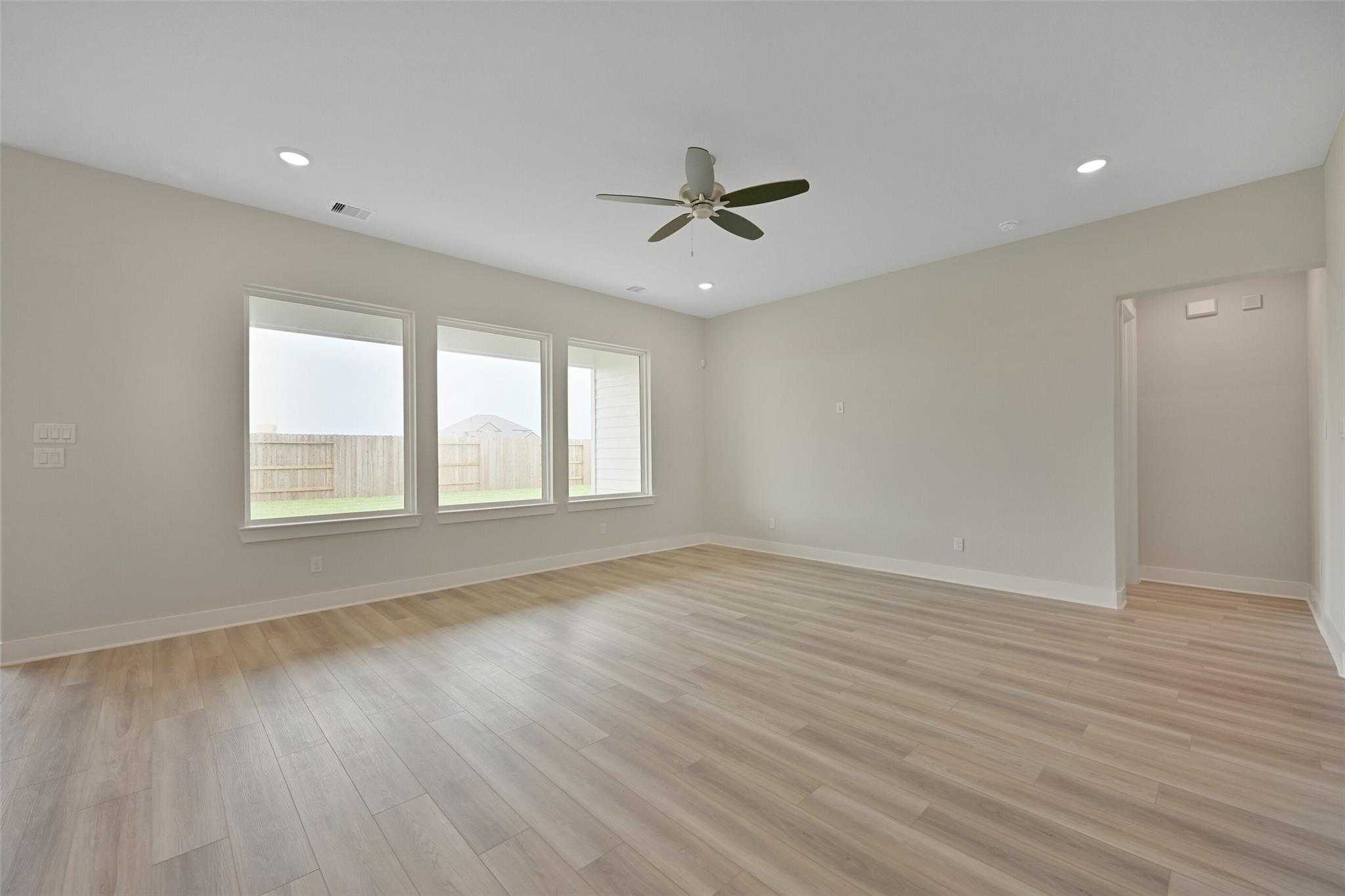 Bright living room with large windows, ceiling fan, light wood floors, and backyard view in Davidson Homes The Edward A, Lago Mar, Texas City
