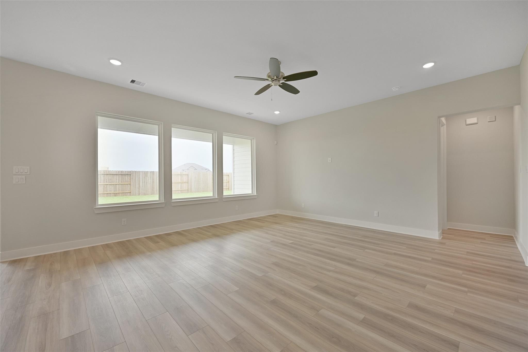 Bright living room with large windows, ceiling fan, light wood floors, and backyard view in Davidson Homes The Edward A, Lago Mar, Texas City