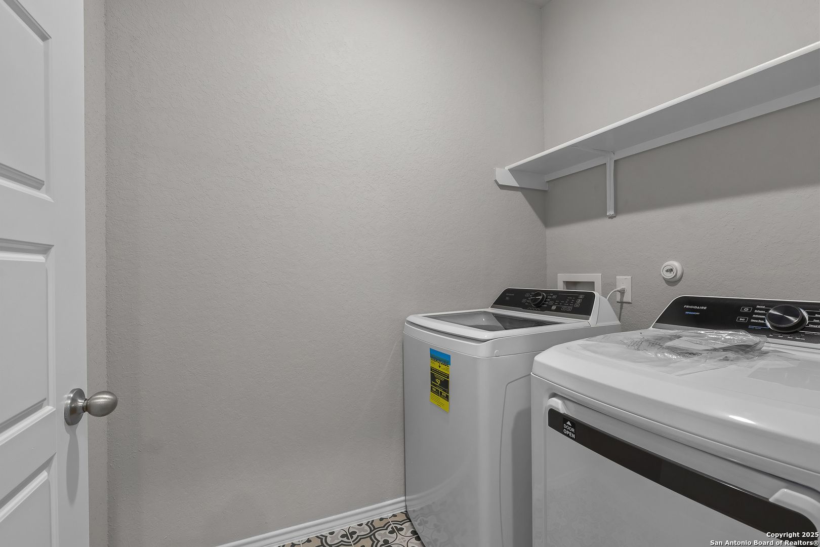 Modern laundry room featuring white front-load washer and dryer, open shelving in Davidson Homes The Colorado B, San Antonio, Texas
