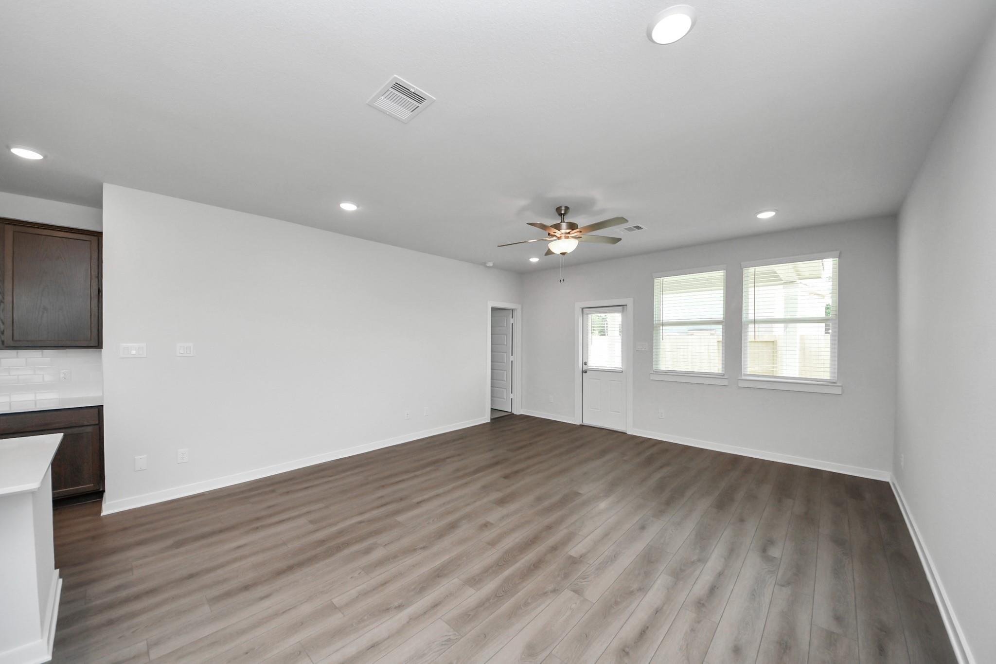 Spacious open-concept living room with wood-style flooring in The Brazos F floor plan, Liberty Estates, Cleveland, Texas.