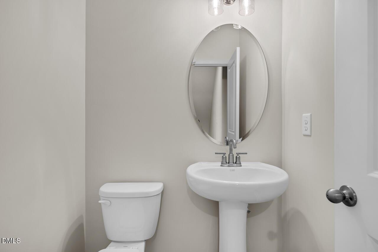 Modern half bath with white pedestal sink, round mirror, and toilet in Davidson Homes The Avery, Knightdale, NC
