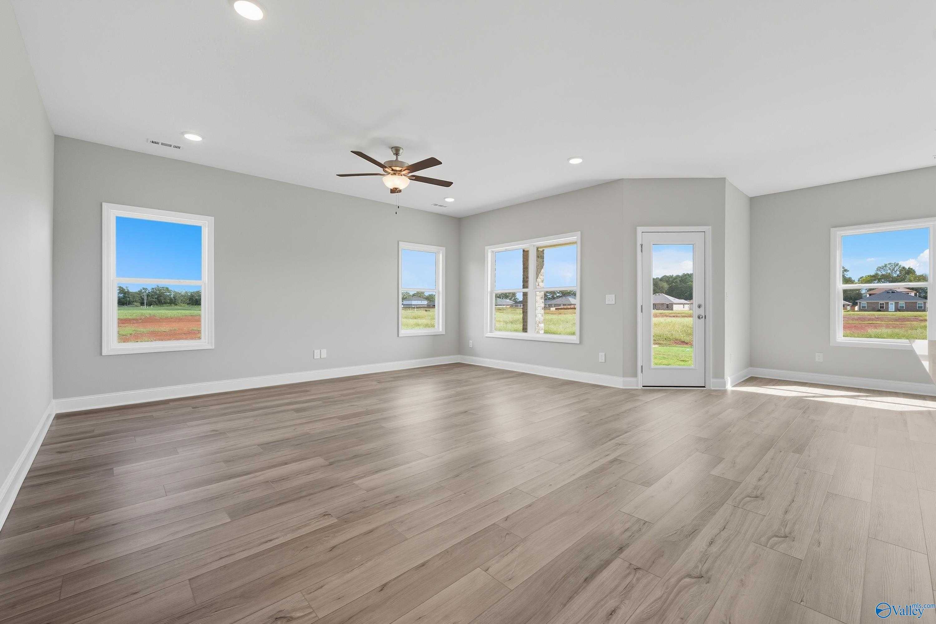 Bright living room with large windows, ceiling fan, and green field views in The Franklin 3-bedroom home, Meridianville, Alabama