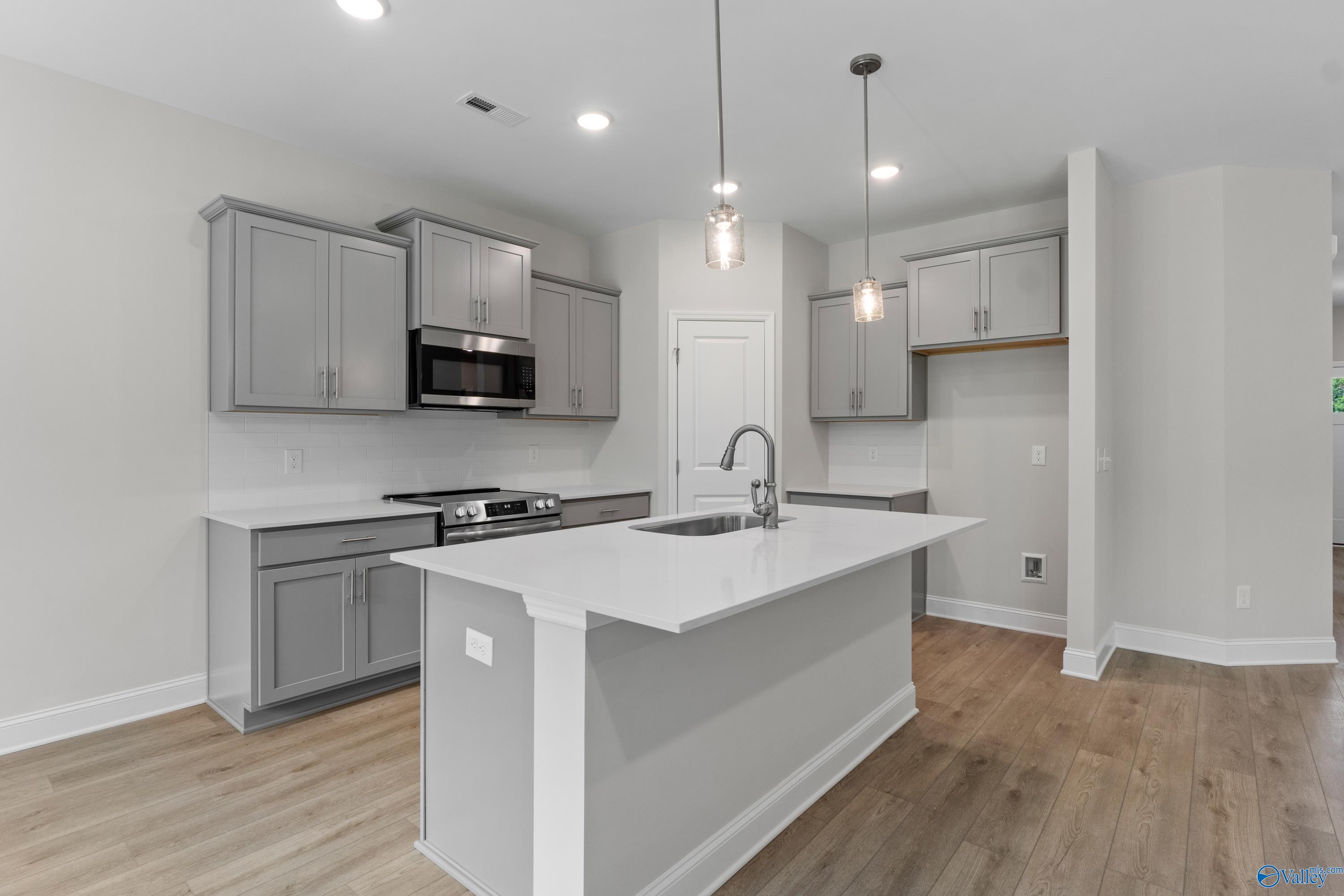 Modern gray cabinet kitchen with white quartz island, stainless appliances, and pendant lights in The Asheville plan, Huntsville AL