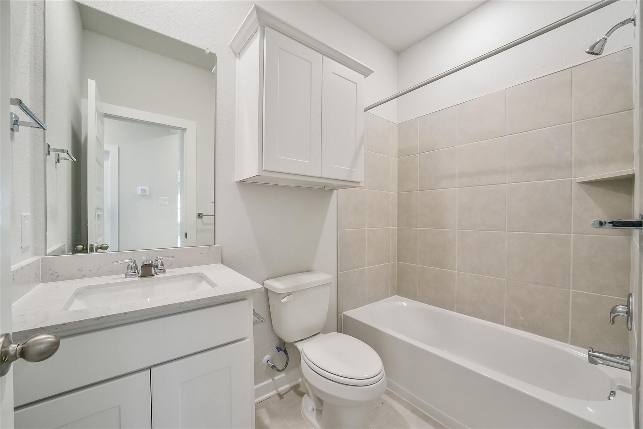 Bright secondary bathroom with white vanity, soaking tub, and neutral tile in Davidson Homes The Frio F, Conroe, Texas