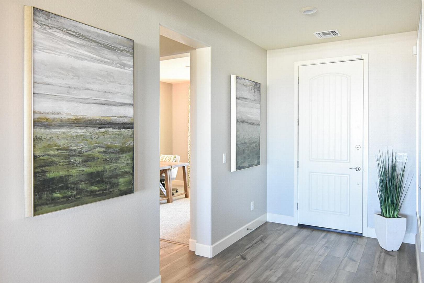 Spacious hallway interior of The Summit E home with abstract green-gray wall art, white door, potted plant, and hardwood floors