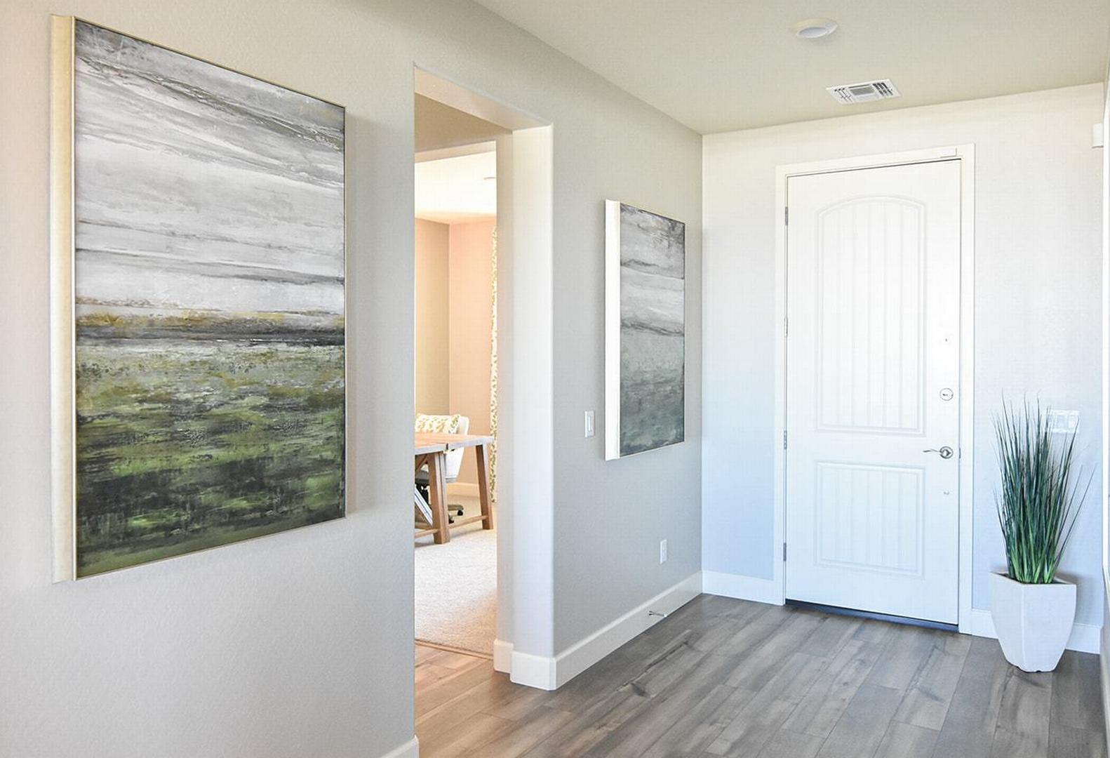 Spacious hallway in The Summit home design featuring abstract wall art, white door, wood flooring, and potted plant