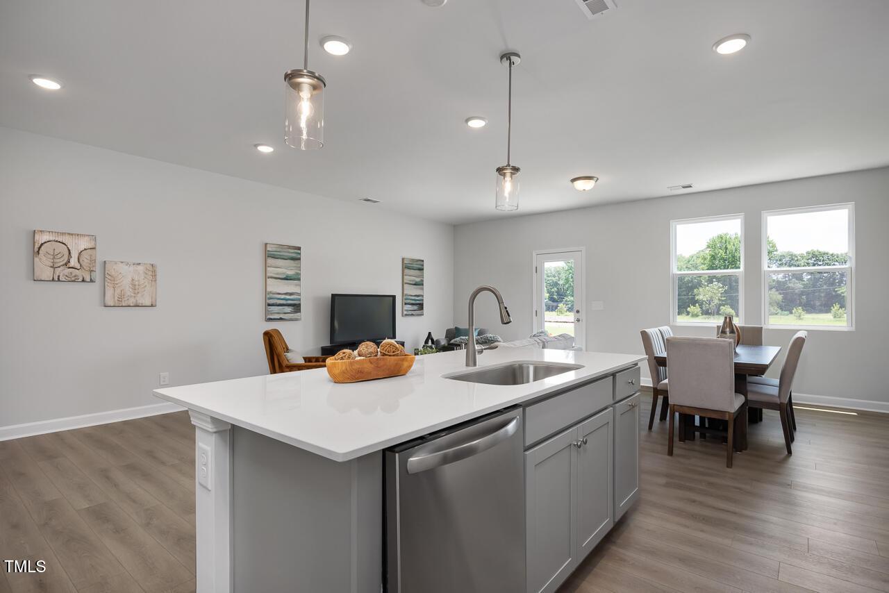 Modern open-concept kitchen with white quartz island, stainless appliances, and dining area in Davidson Homes The Warren, Fuquay-Varina, NC