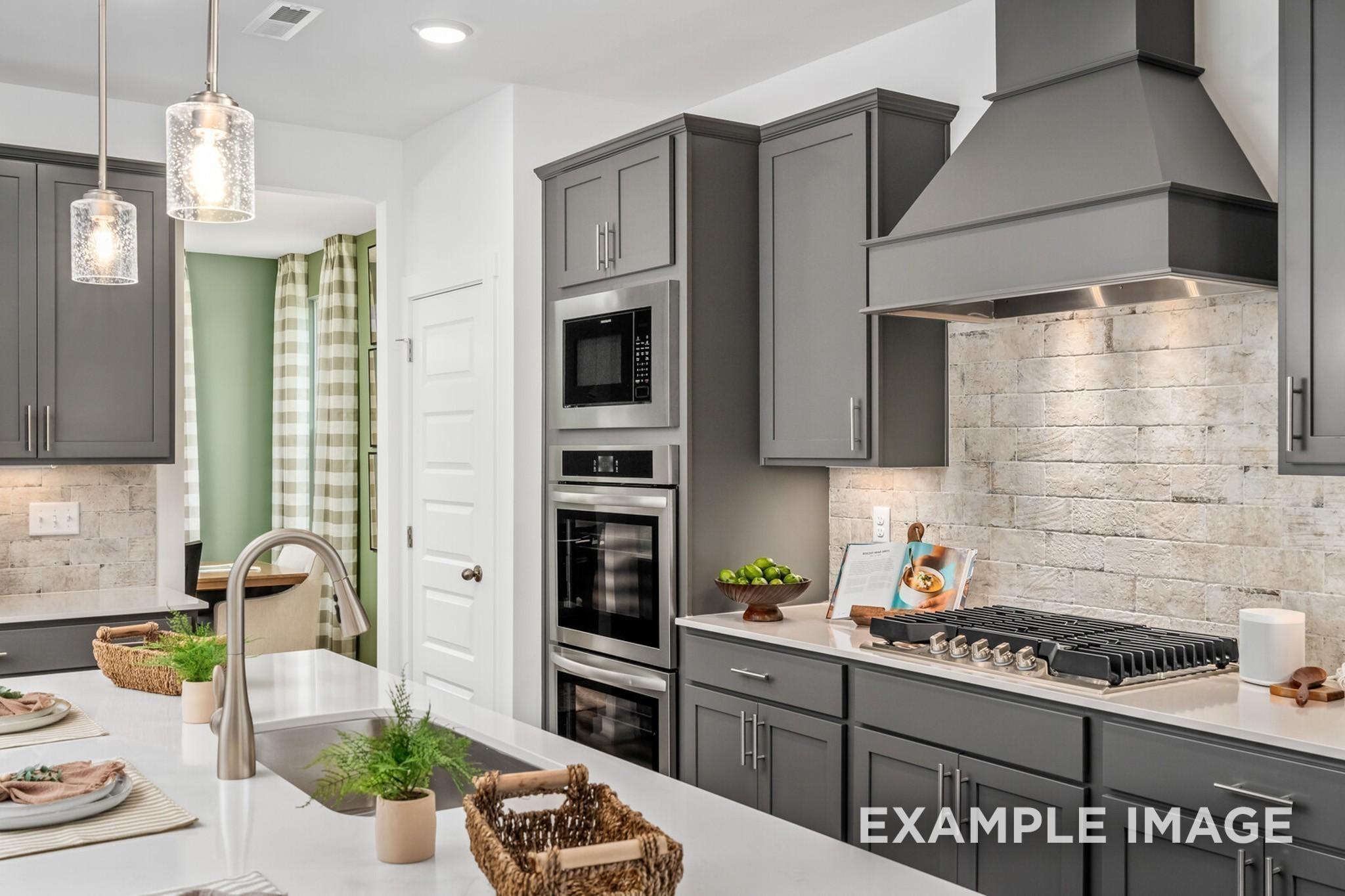 Modern kitchen with grey cabinets, stainless appliances, and brick backsplash in The Ash A floor plan at Woods Crossing.