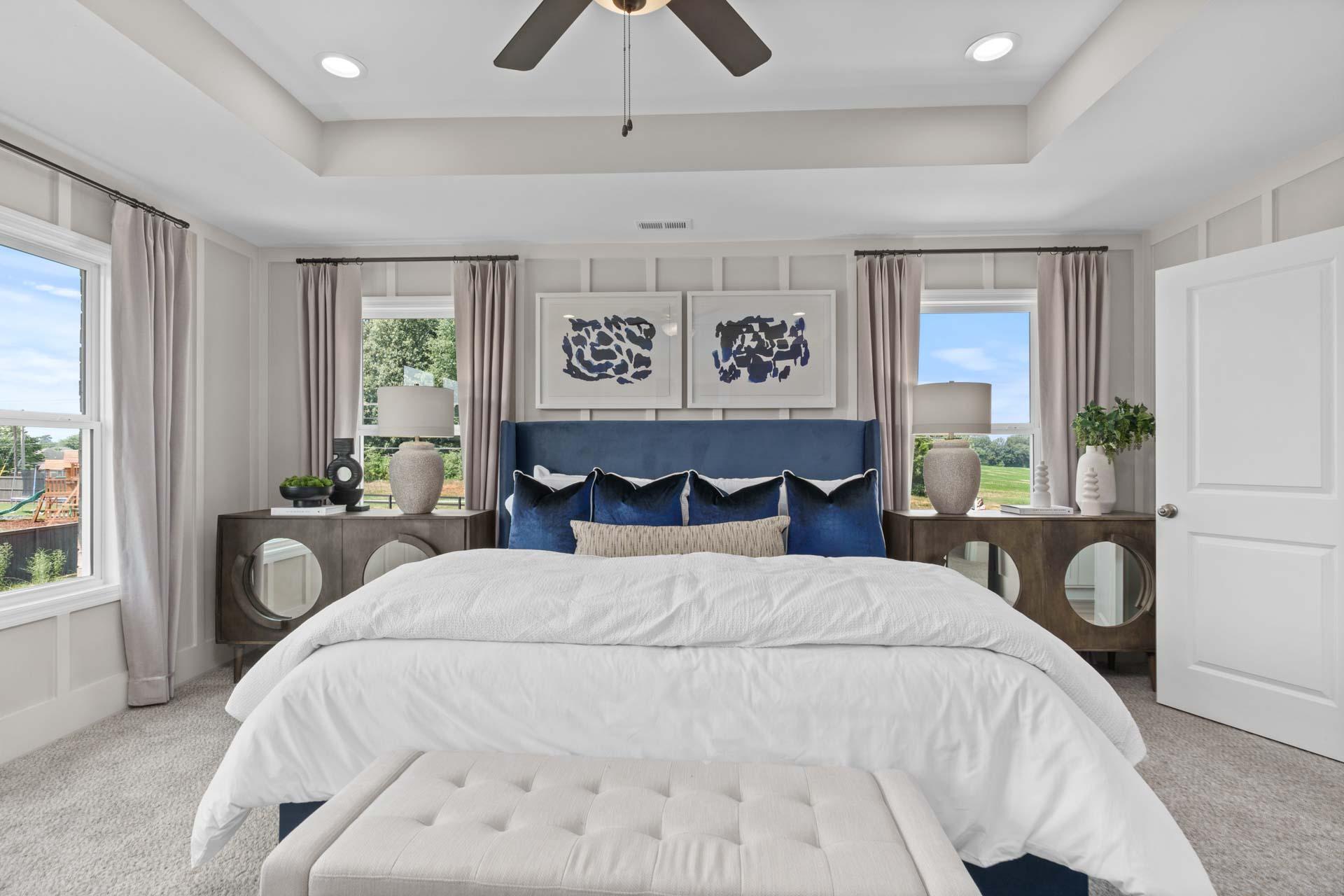 Elegant master bedroom in Creek Grove, New Market AL with king bed, blue accents, ceiling fan, and large curtained windows