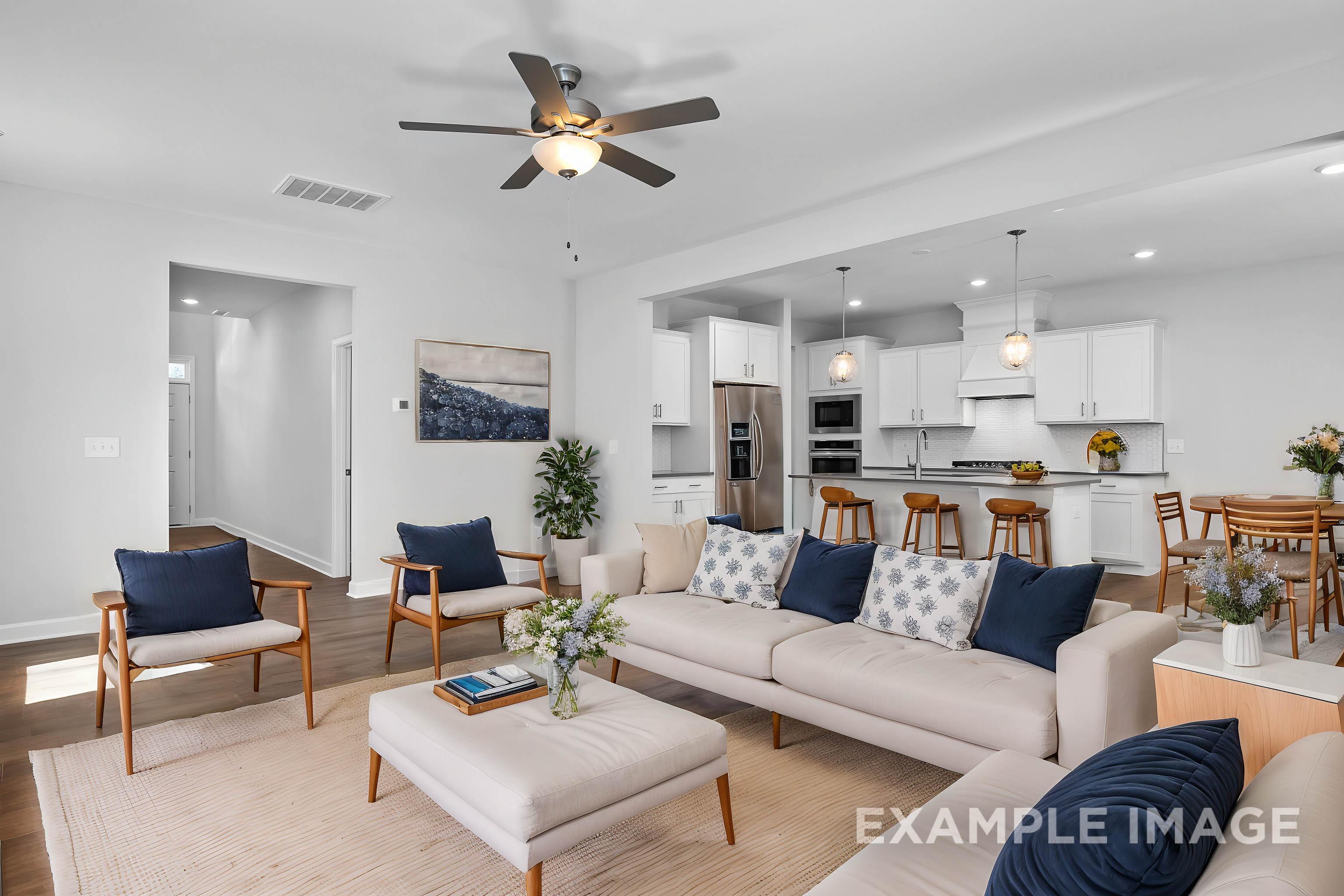 Spacious open-concept living room in The Gavin B with beige sofa, blue accents, wooden chairs, and adjacent modern kitchen with island