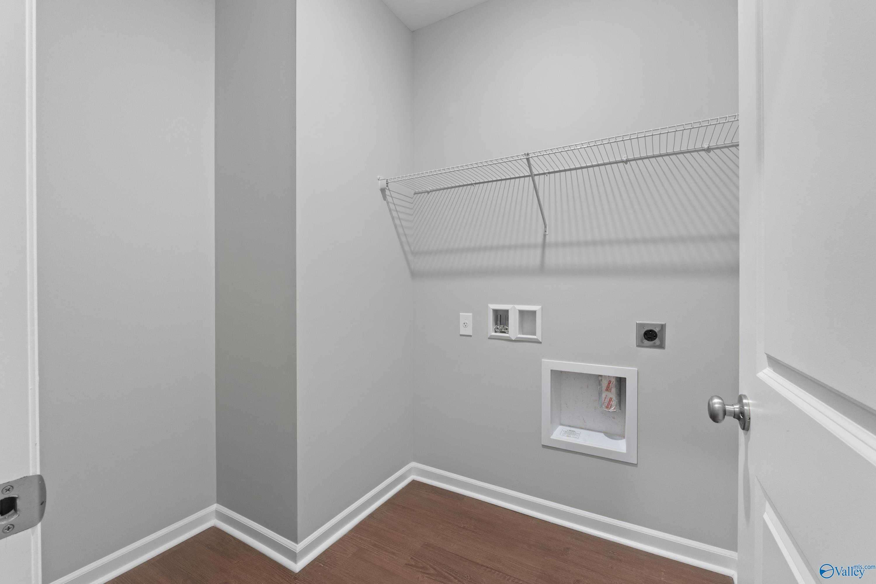 Modern laundry room featuring wire shelving, utility hookups and hardwood floors in Davidson Homes The Stella, Hazel Green, AL
