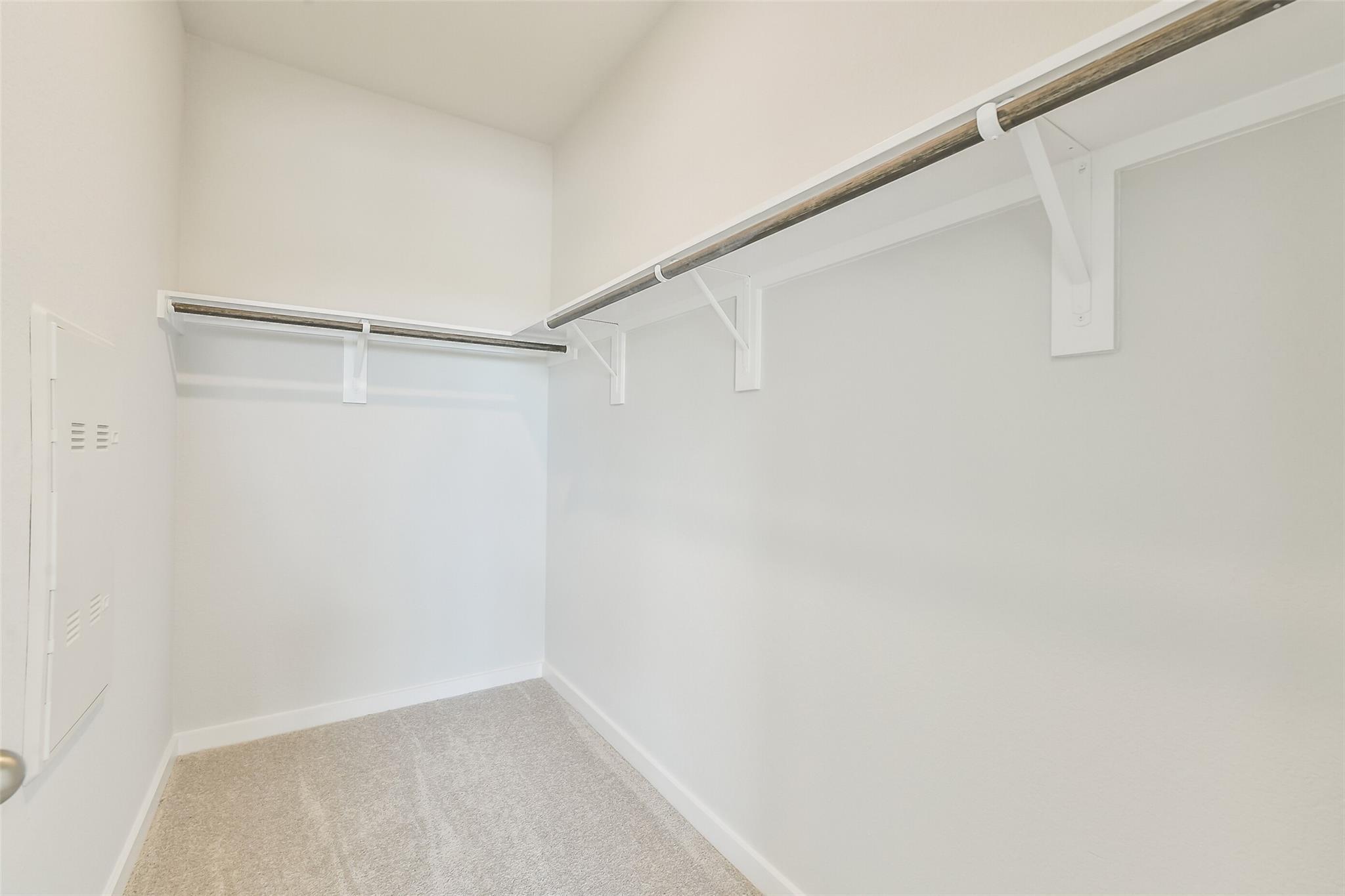 Spacious walk-in closet with wooden hanging rods, white brackets, beige carpet in The Frio G home, Conroe, Texas