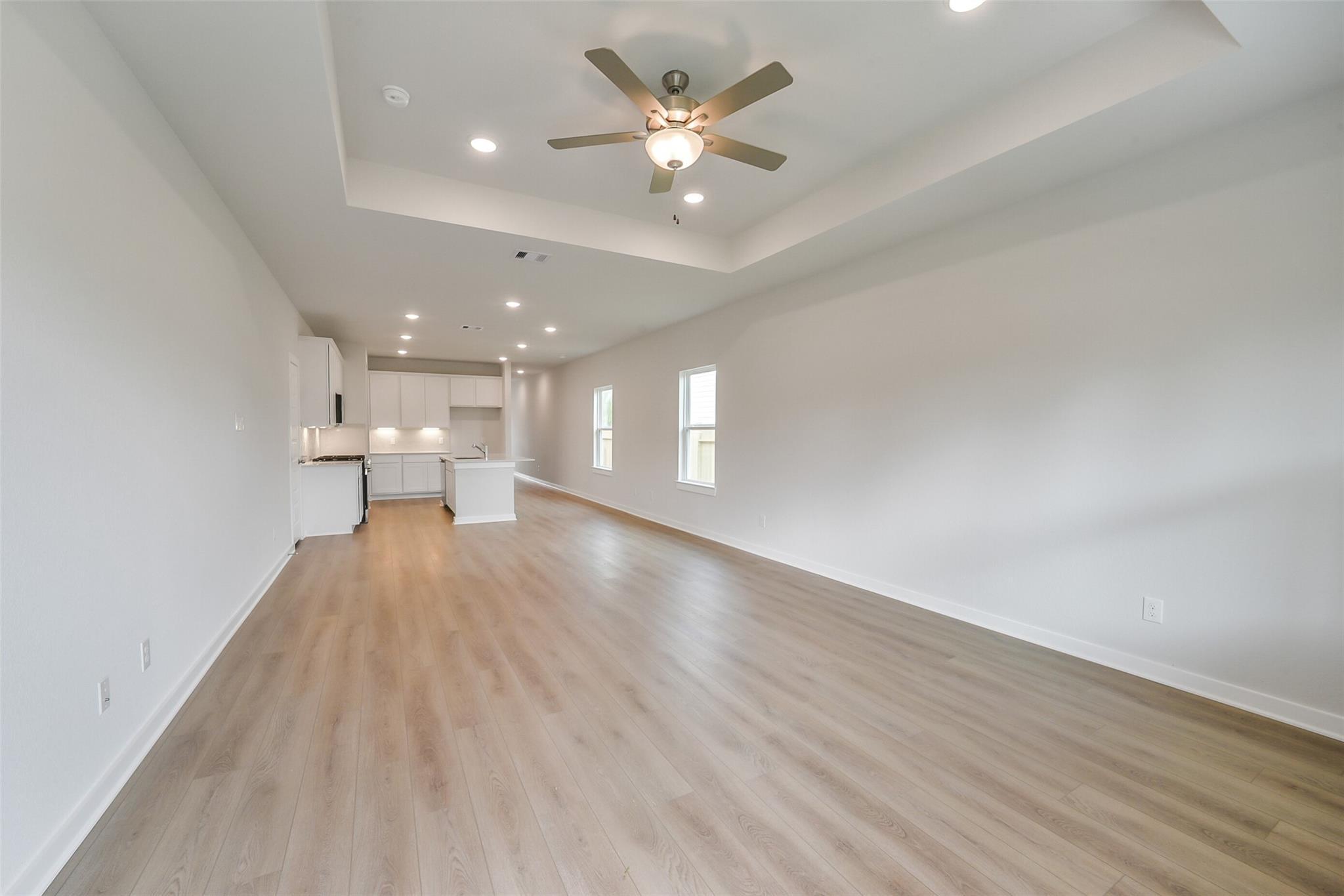 Open-concept hallway to kitchen with white cabinets, tray ceilings, ceiling fans, and hardwood floors in Davidson Homes The Frio F, Conroe, Texas
