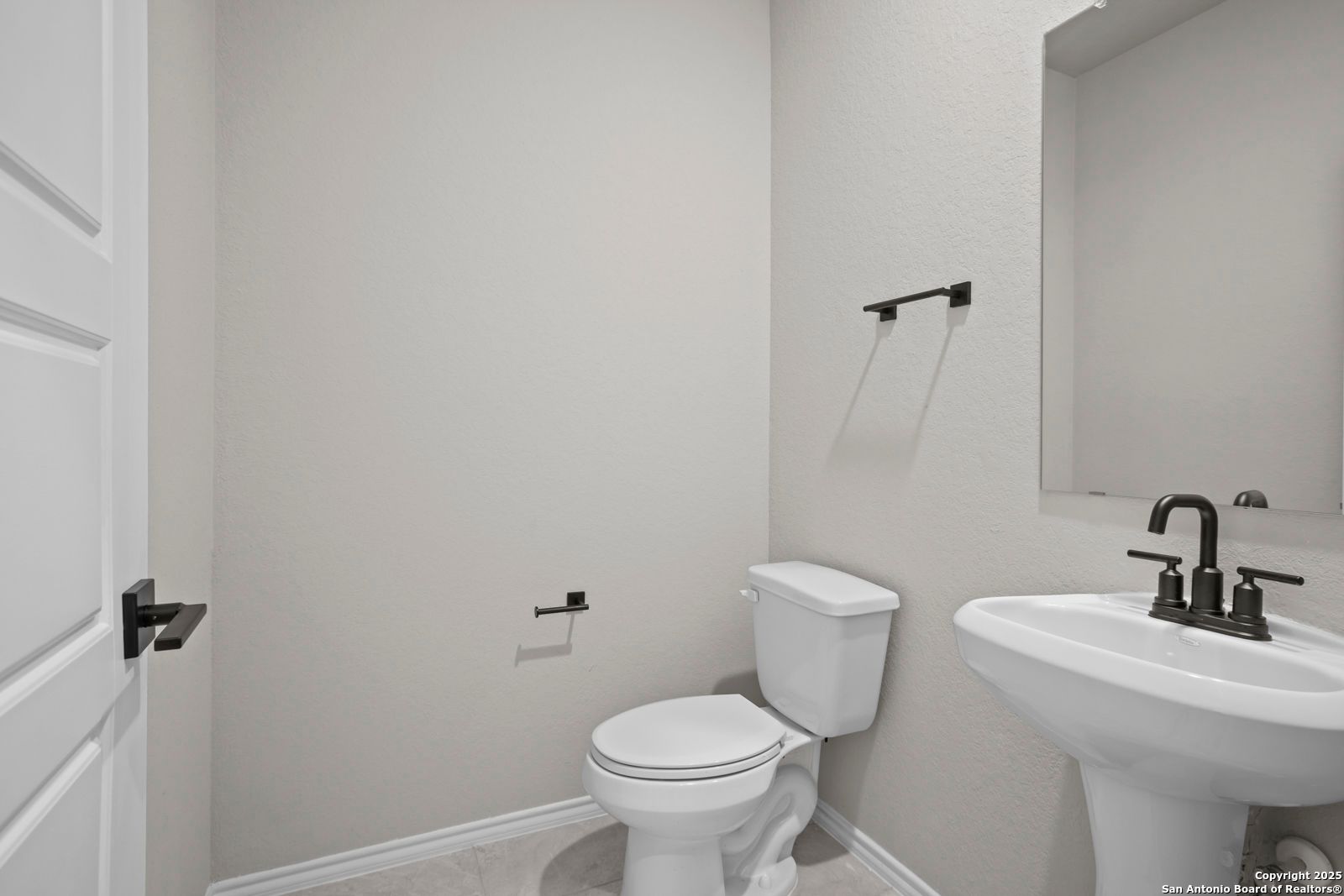 Elegant powder room with white porcelain toilet, sink, black faucet, and mirrored vanity in Davidson Homes The Sequoia A, Converse, Texas