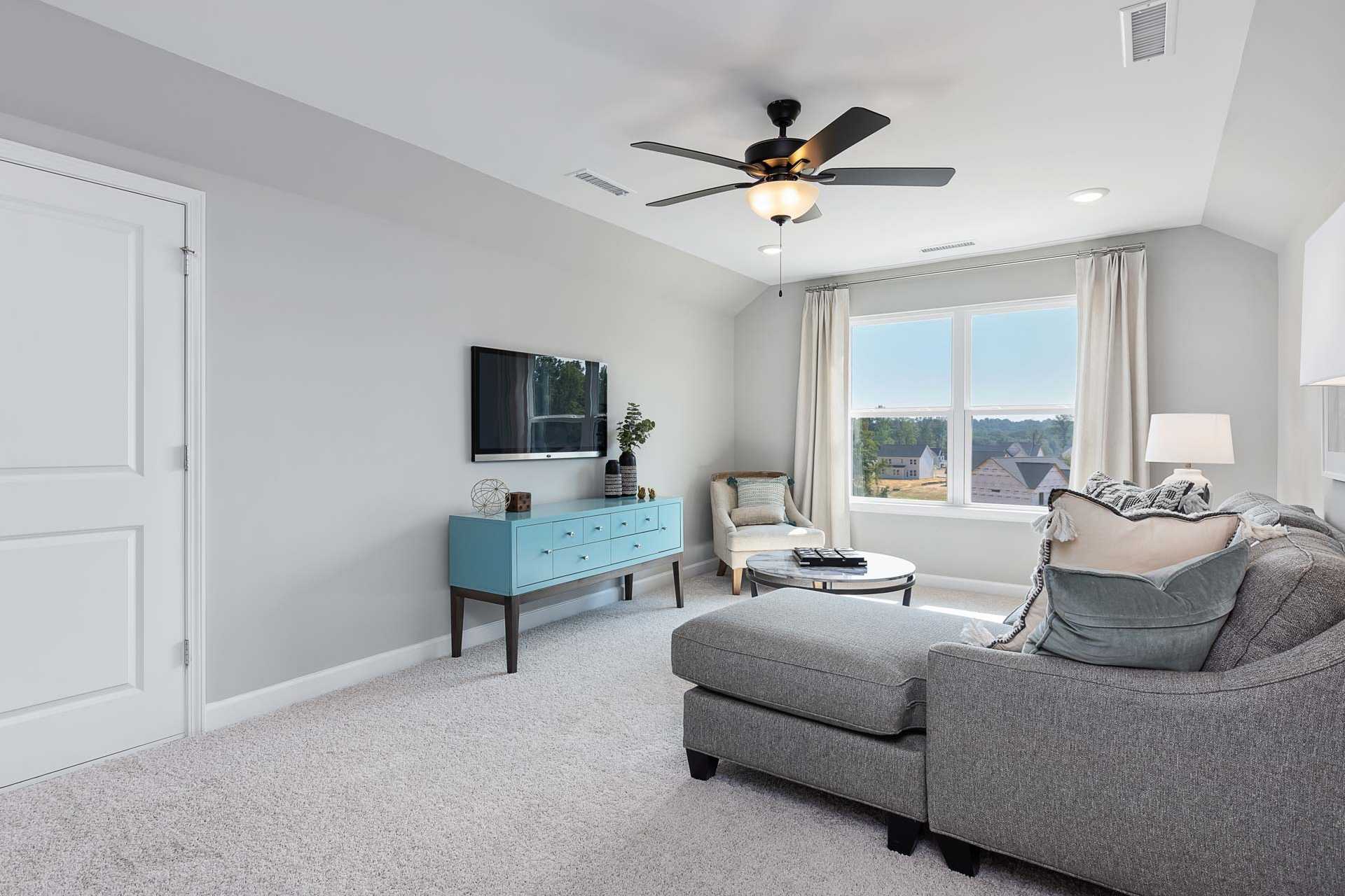 Cozy bonus room at Highland Forest in Fuquay-Varina NC with gray sectional sofa, armchair, TV, and large window view