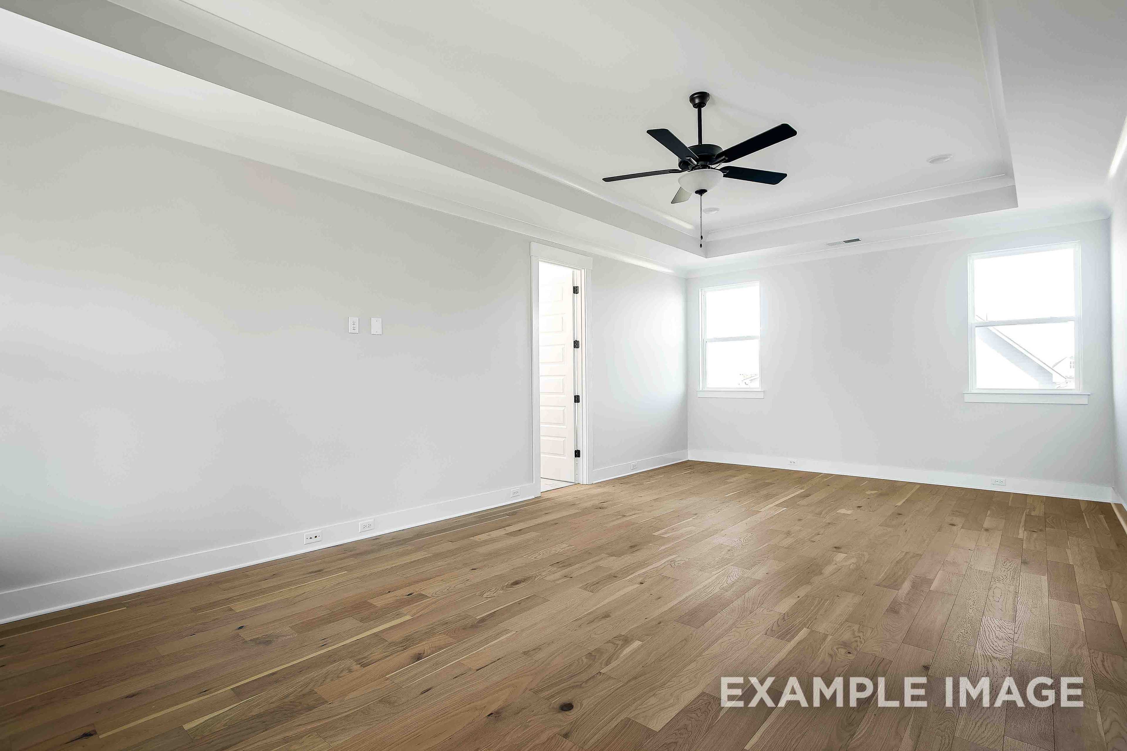 Spacious master suite in The Alston A featuring hardwood floors, ceiling fan, and large windows