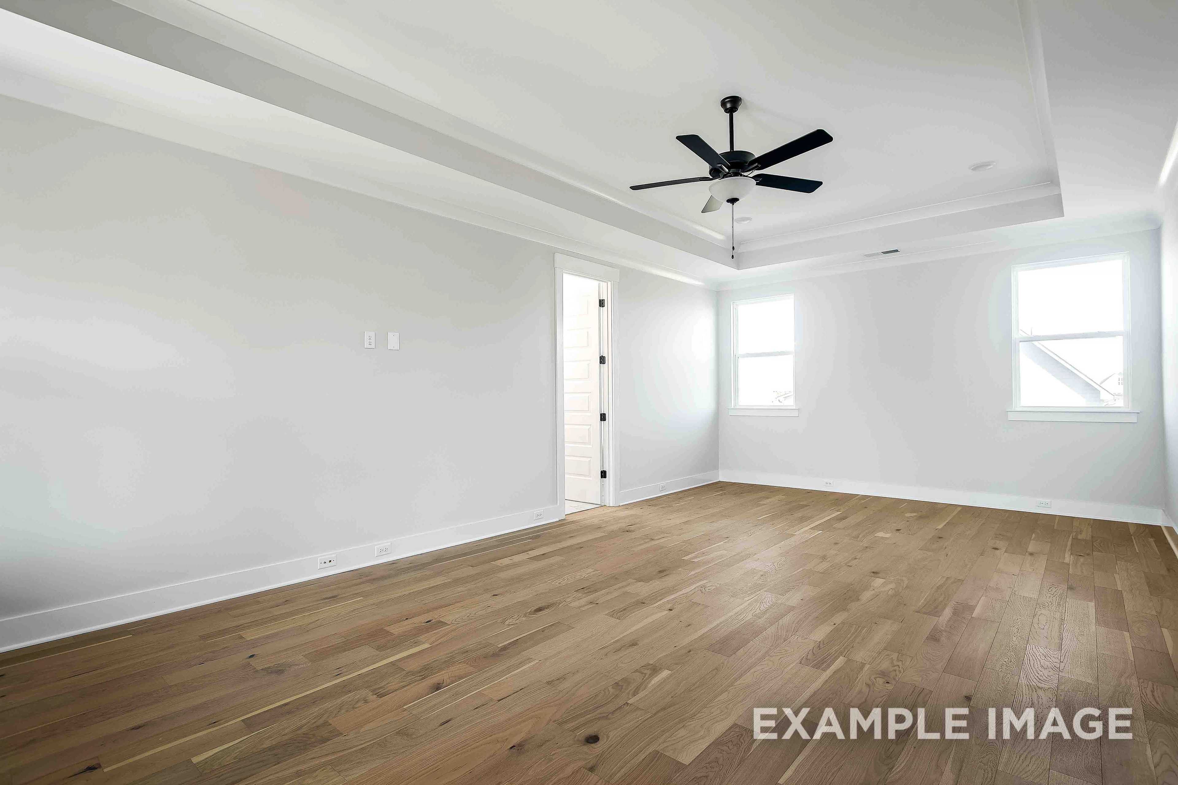 Spacious master suite in The Alston A featuring hardwood floors, ceiling fan, and large windows