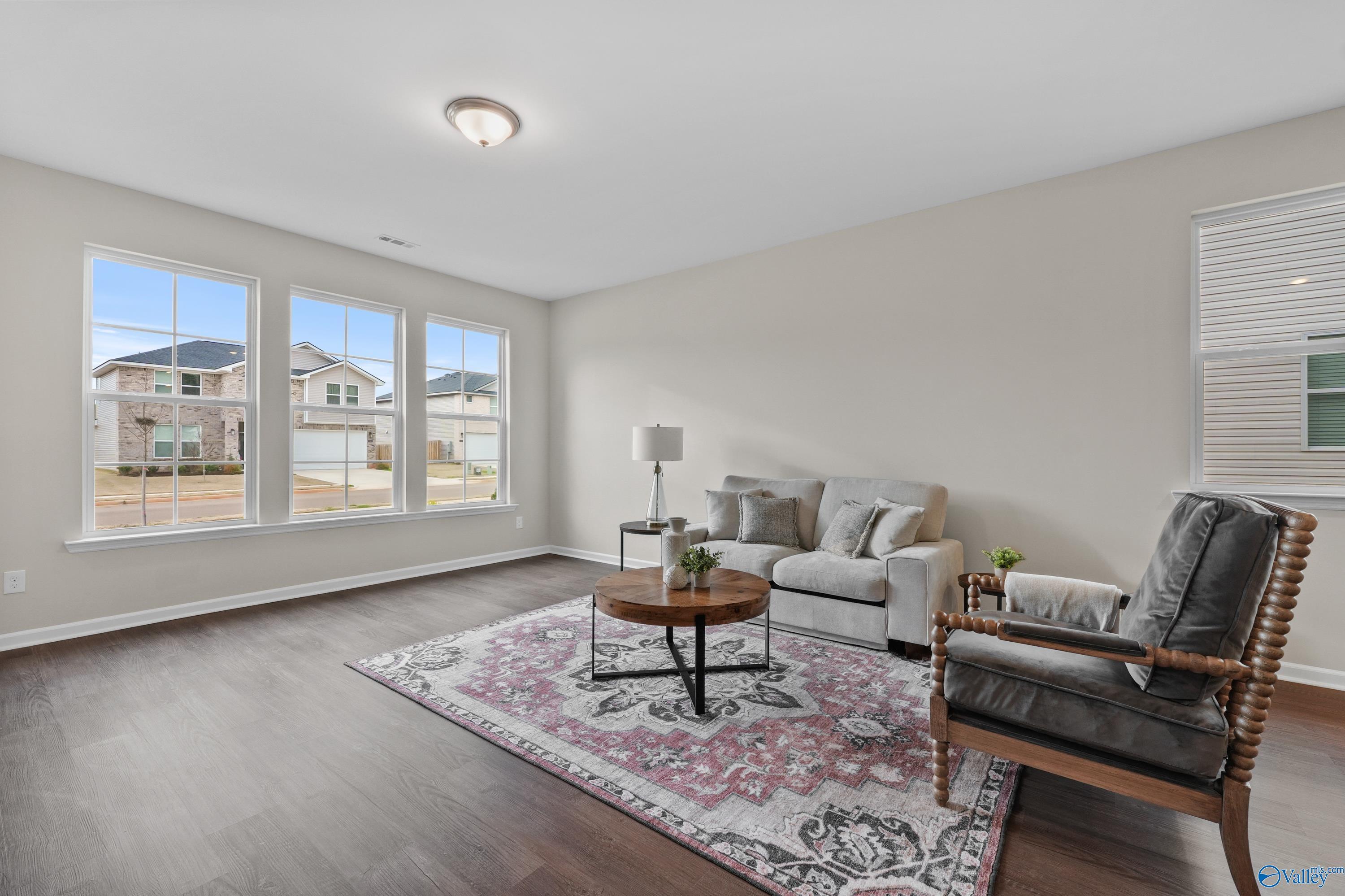 Cozy living room with beige sofa, gray armchair, wooden coffee table, plant, and large windows in Davidson Homes The Stella, Hazel Green, Alabama