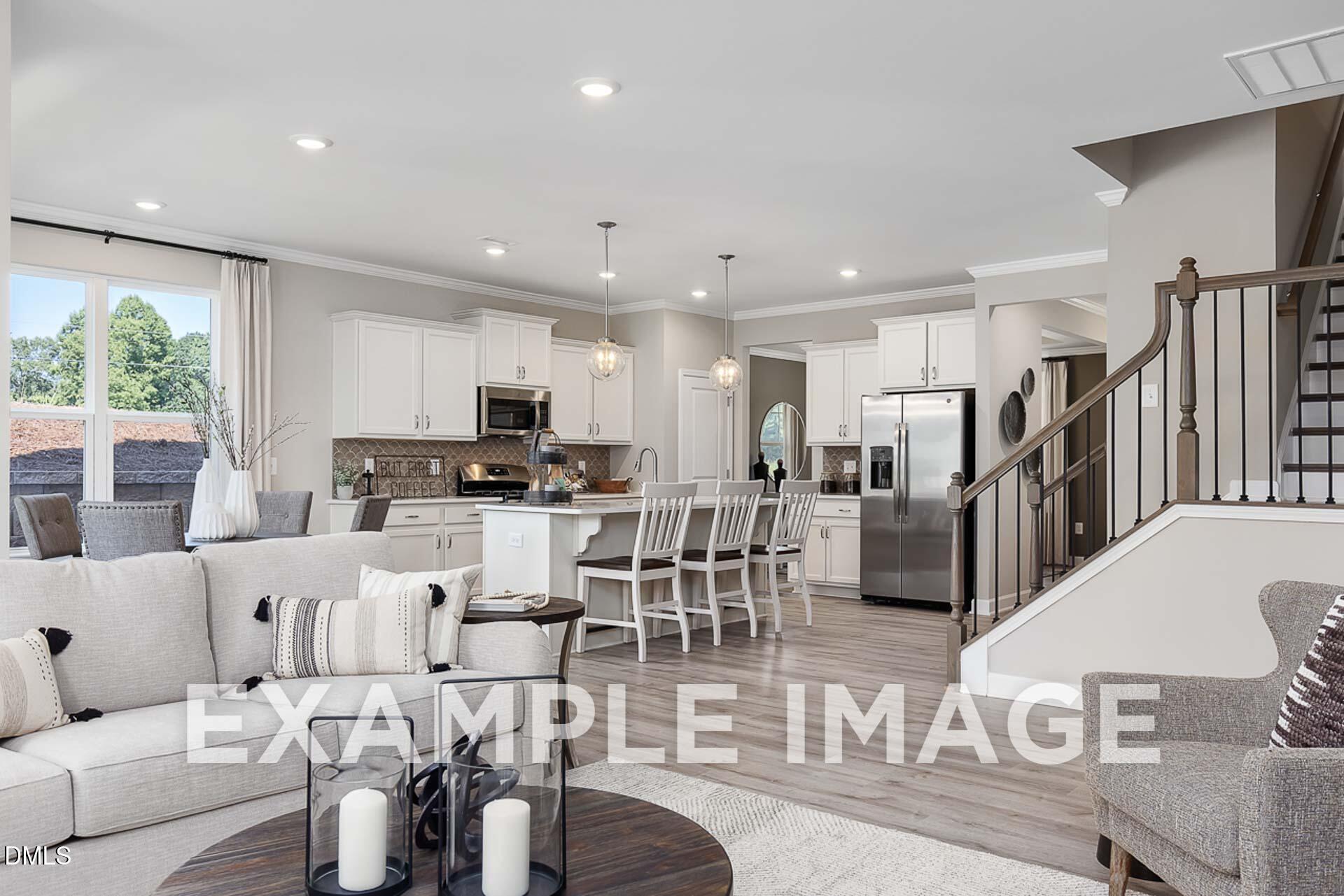 Open-concept living room and kitchen with white cabinets, stainless fridge, island seating, and gray sofa in The Ash B by Davidson Homes, Lillington, NC