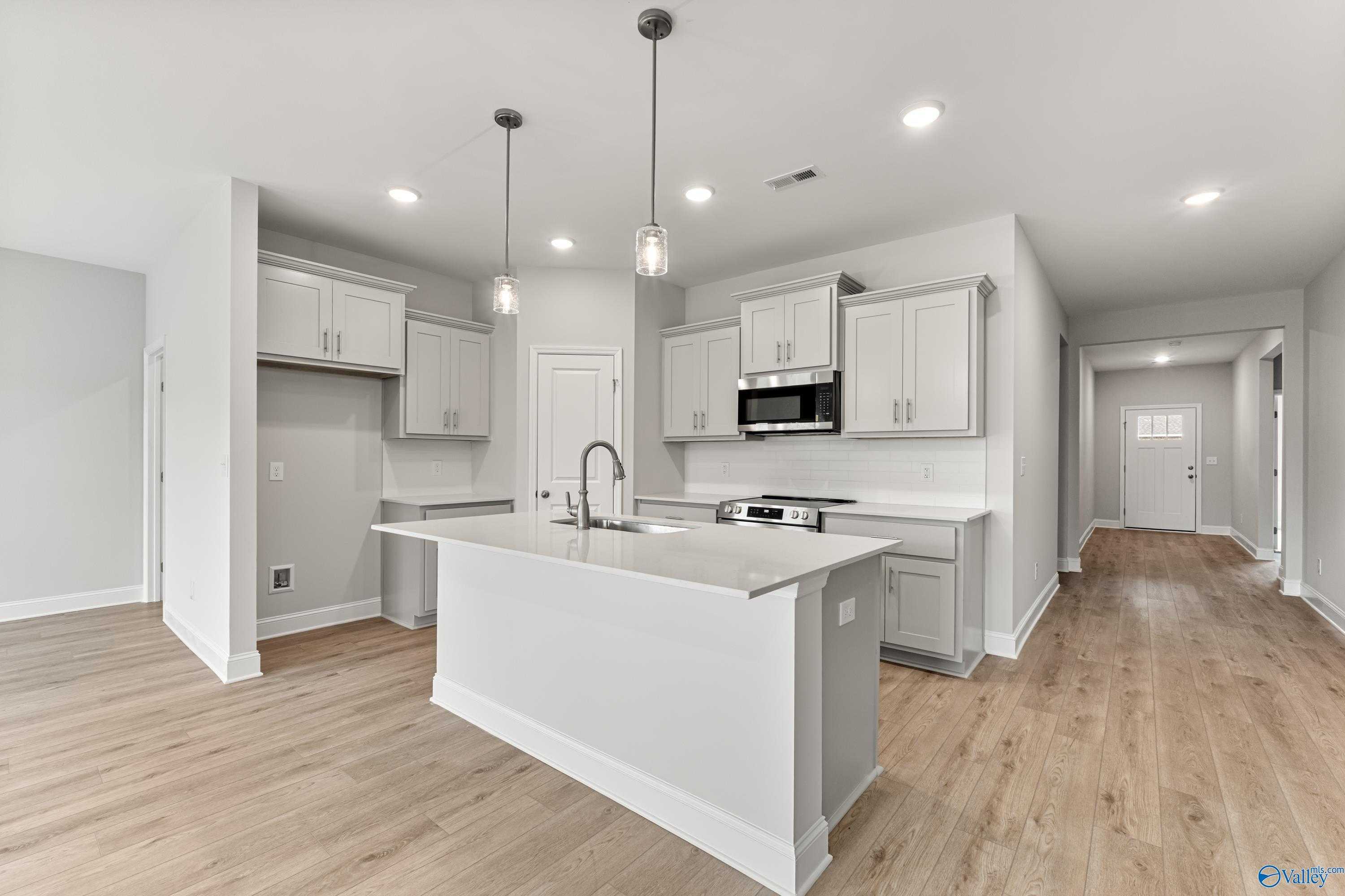 Modern white shaker kitchen with large island sink, stainless steel range, pendant lights in Davidson Homes Daphne C, Athens AL
