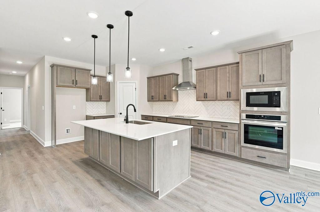 Modern kitchen with large island, taupe cabinetry, stainless appliances, and pendant lights in Davidson Homes Rockford plan, Hartselle AL