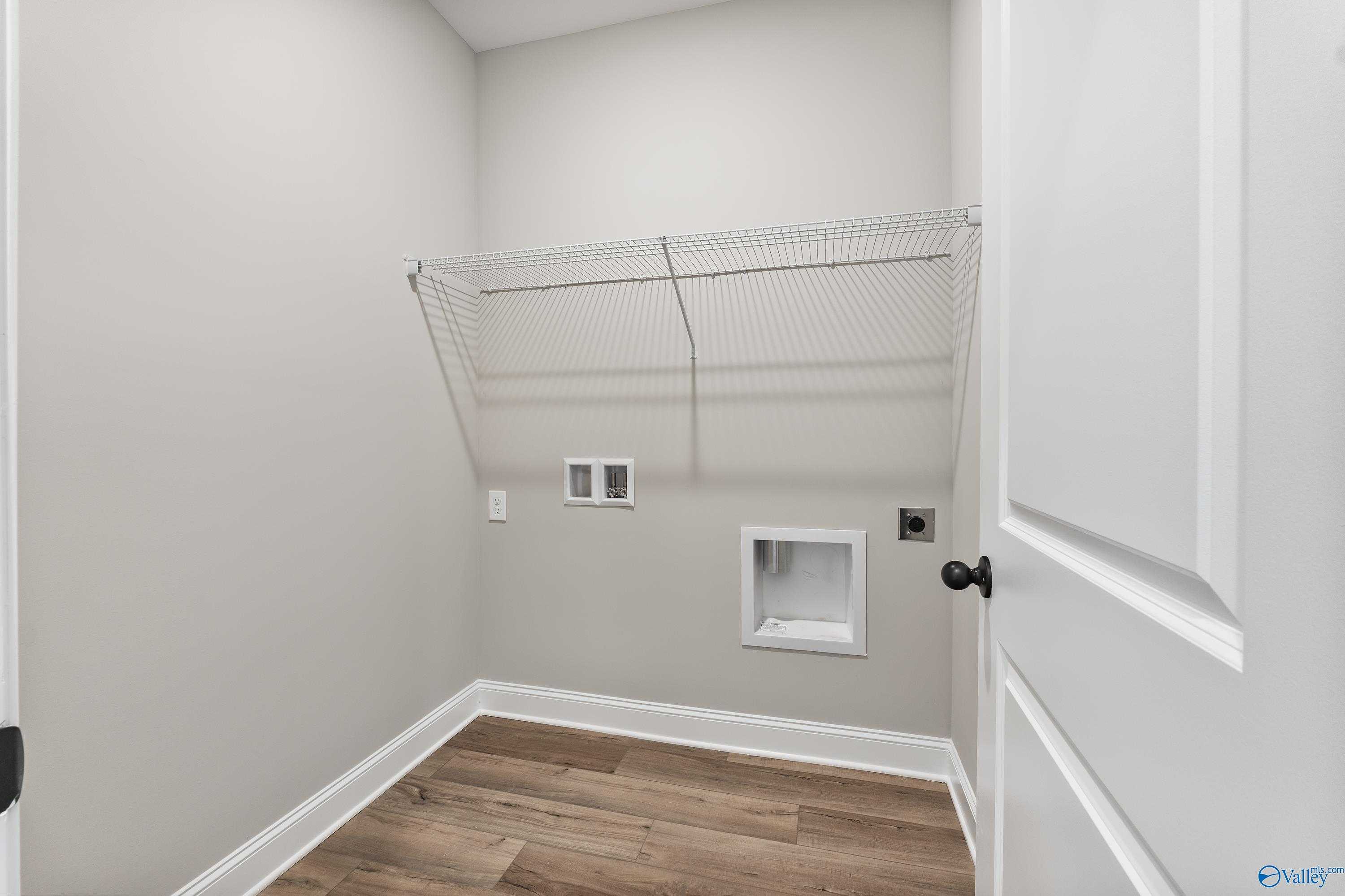 Modern laundry room featuring wire shelving, washer-dryer hookups, and hardwood floors in Davidson Homes The Franklin B, Hazel Green, Alabama