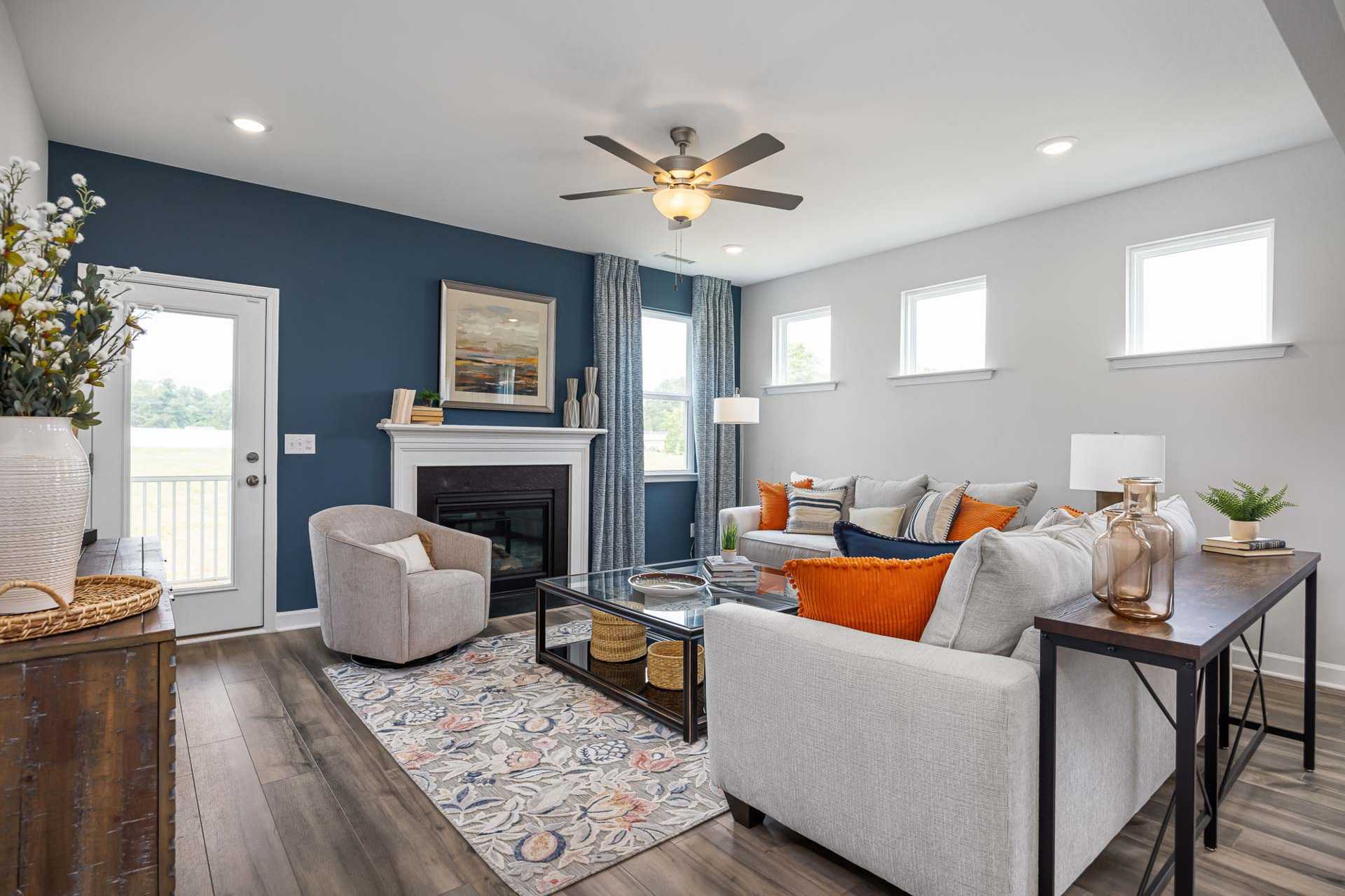 Cozy living room in Beverly Place, Four Oaks NC with navy accent wall, white fireplace, gray sectional sofa, hardwood floors and ceiling fan