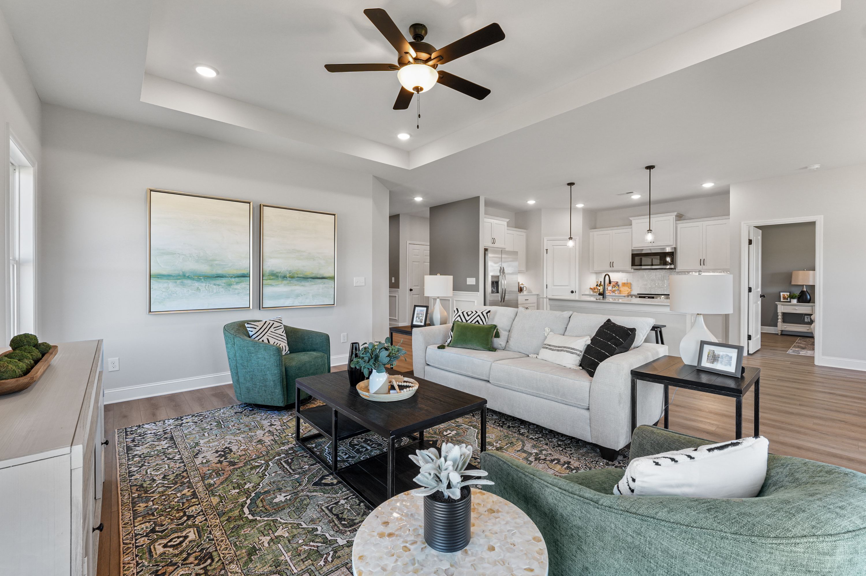 Open-concept living room in Ramsay Cove home, Owens Cross Roads AL with white sofa, green chairs, abstract art and adjacent kitchen