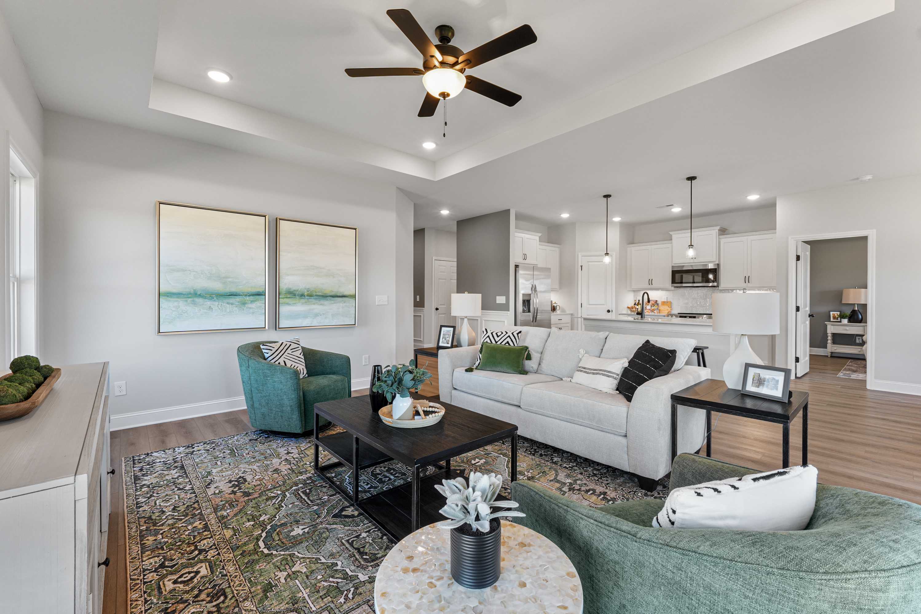 Open-concept living room in Ramsay Cove home, Owens Cross Roads AL with white sofa, green chairs, abstract art and adjacent kitchen