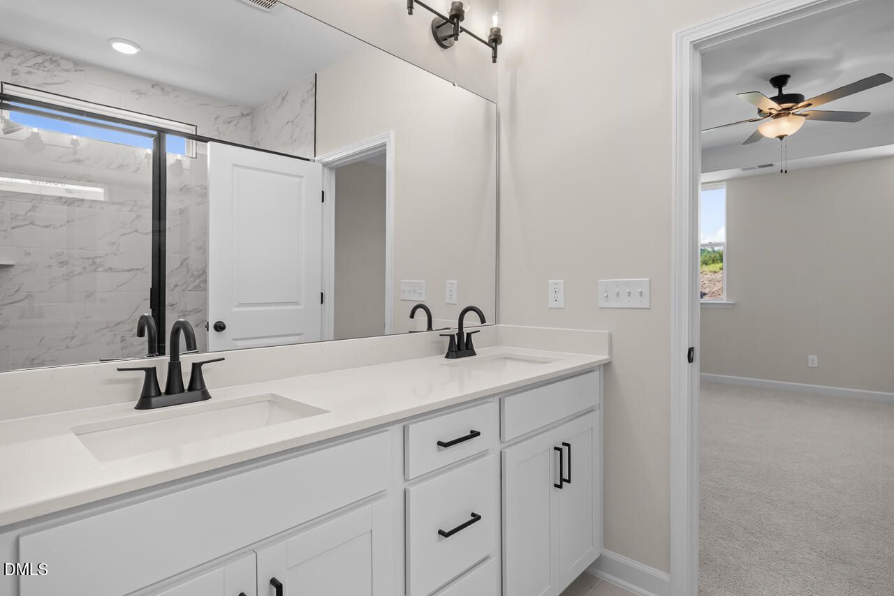 Double vanity bathroom with white cabinets, black fixtures, and marble tile shower in Davidson Homes Ashport M, Wendell Ridge NC