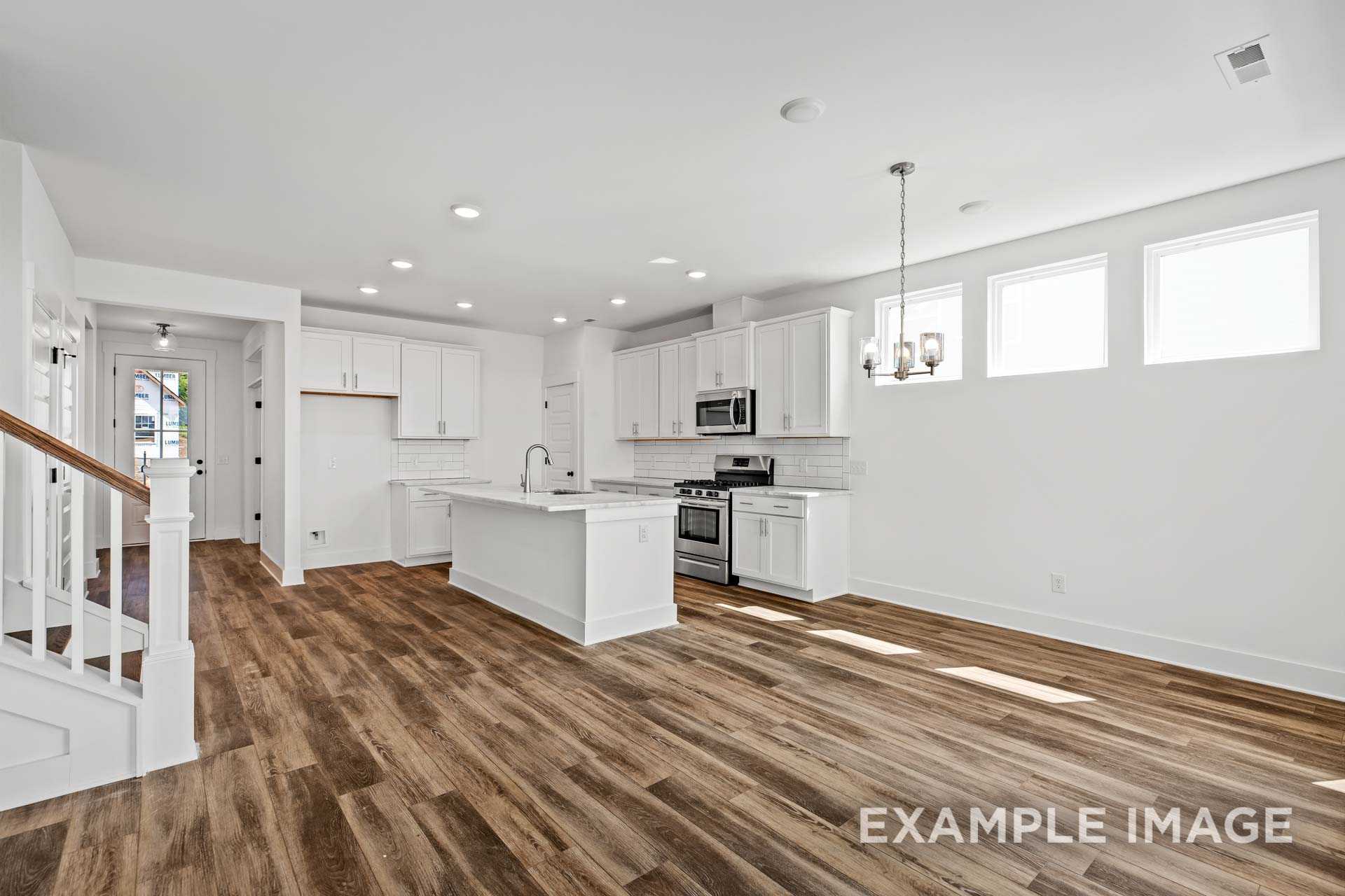 Spacious kitchen in The Ash C Davidson Homes plan featuring white cabinets, large island with sink, stainless appliances, pendant lights, and hardwood floors