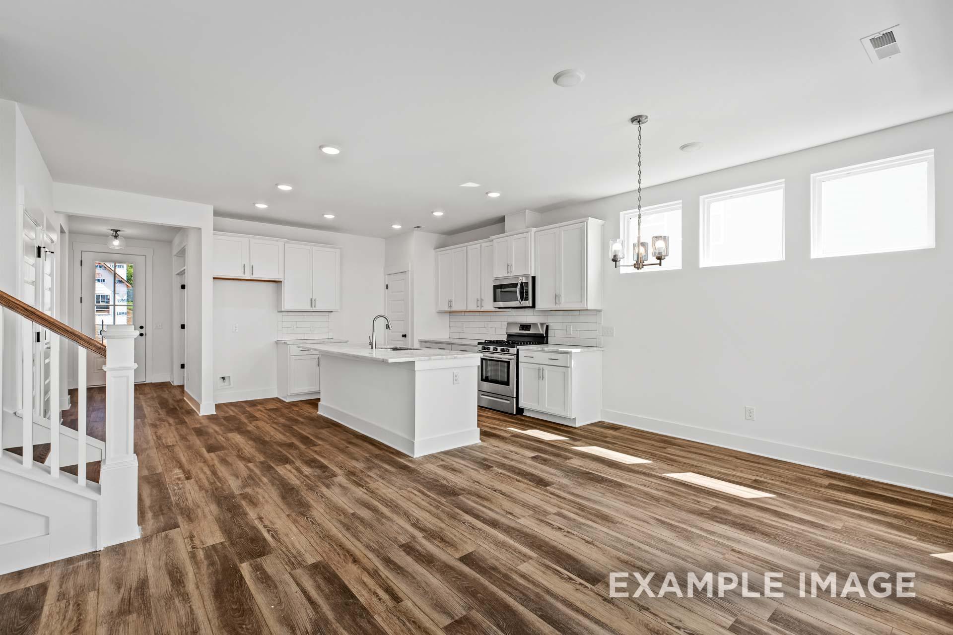 Spacious kitchen in The Ash C Davidson Homes plan featuring white cabinets, large island with sink, stainless appliances, pendant lights, and hardwood floors