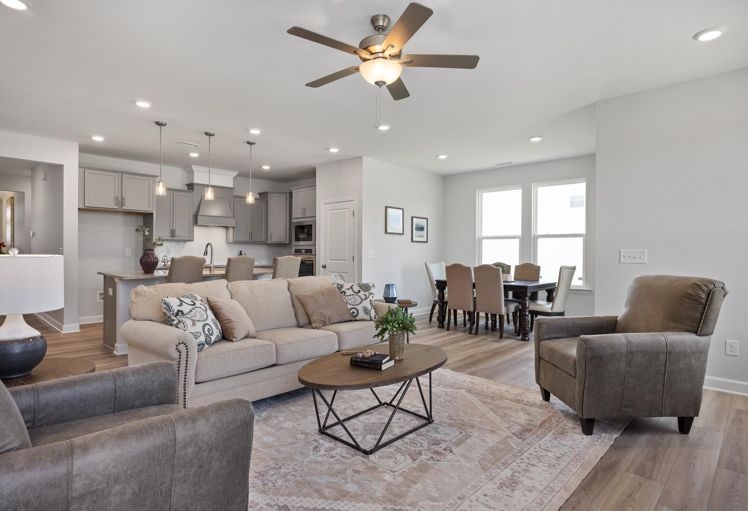 Spacious open-concept living and dining area in The Daphne C with modern gray kitchen island, beige sofa, wooden table, and ceiling fan