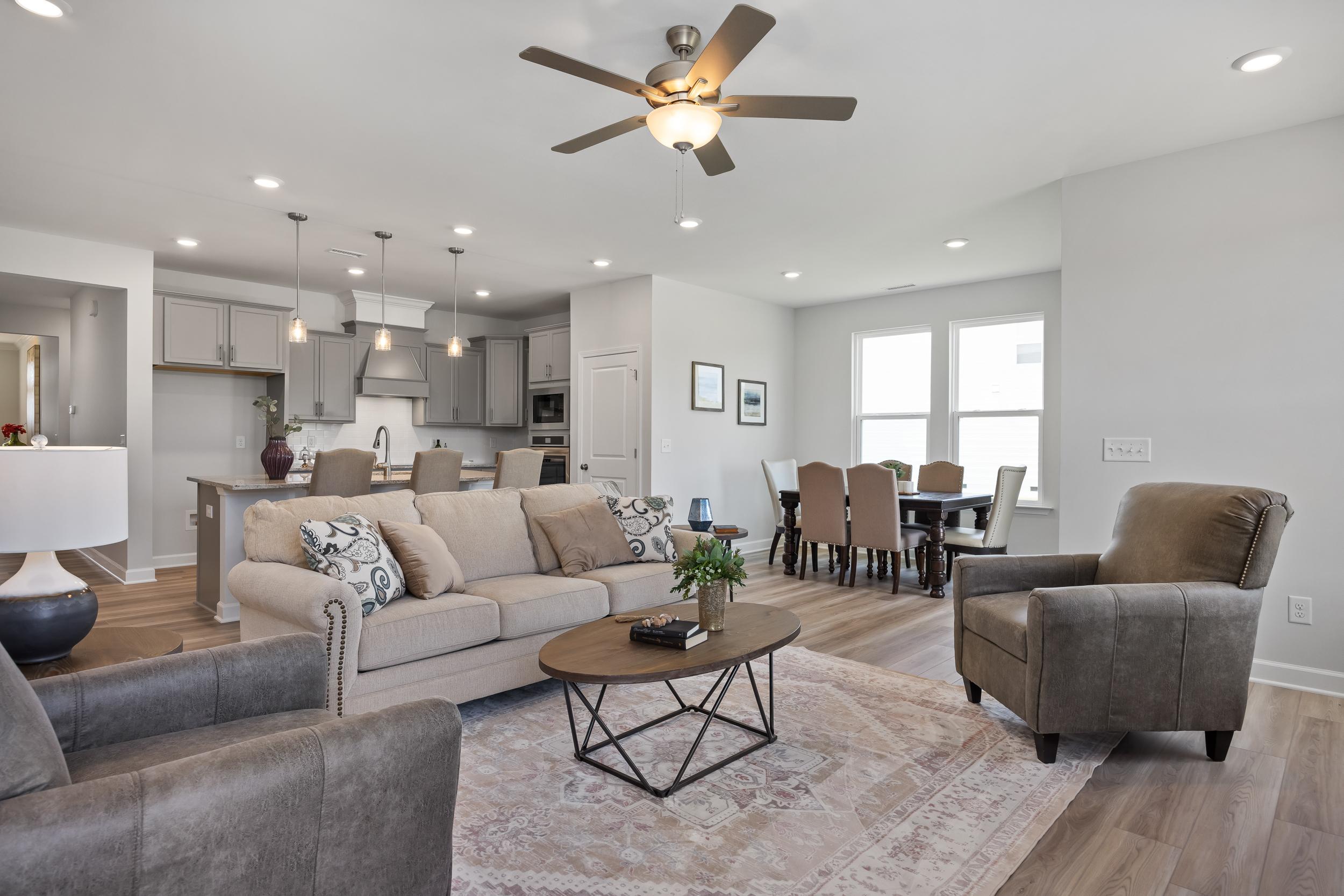 Spacious open-concept living and dining in The Daphne D with gray sofas, wood floors, ceiling fan, and modern kitchen island