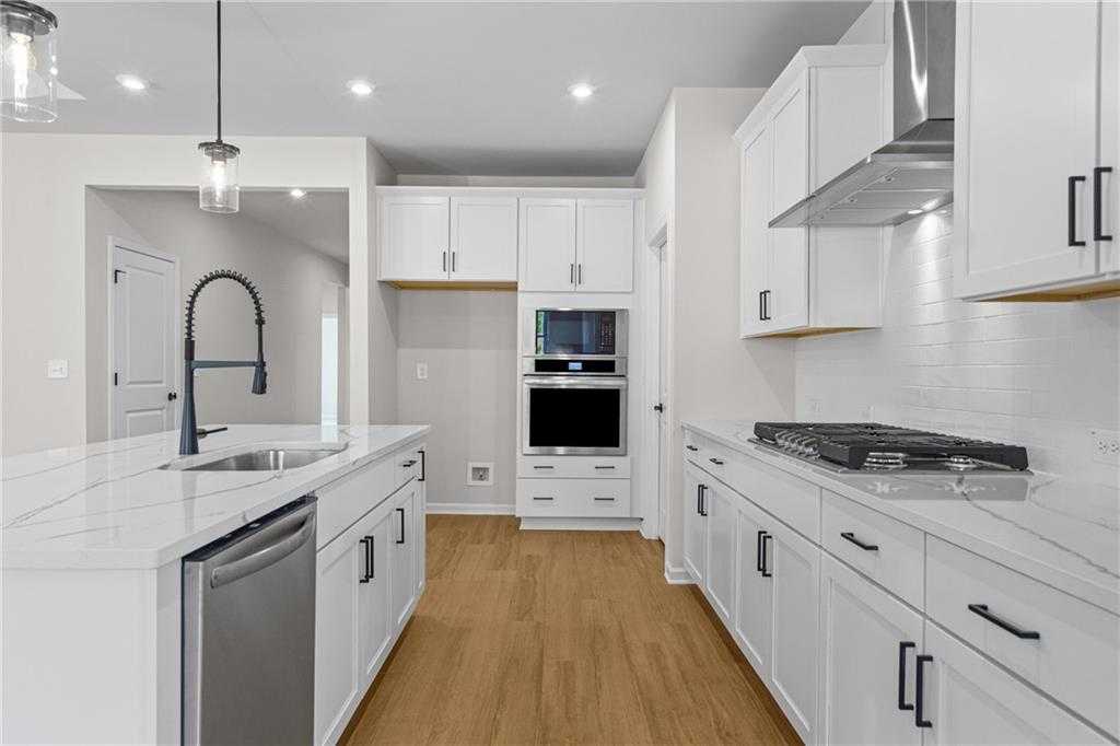 Modern white shaker kitchen with quartz island, stainless appliances, and hardwood floors in Davidson Homes The Edison A, Loganville, GA