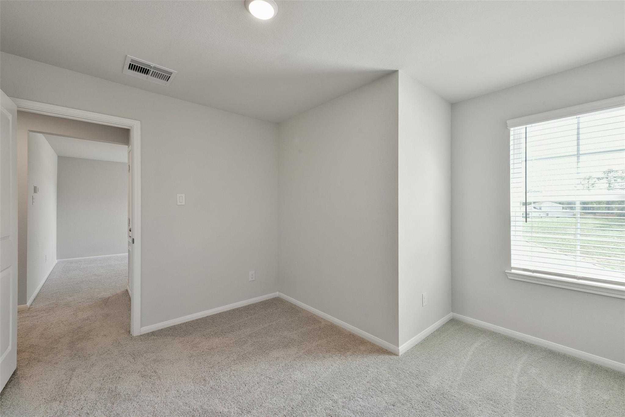 Spacious empty bedroom with neutral beige walls, berber carpet, and large window in Davidson Homes Sabine E, Dayton, Texas
