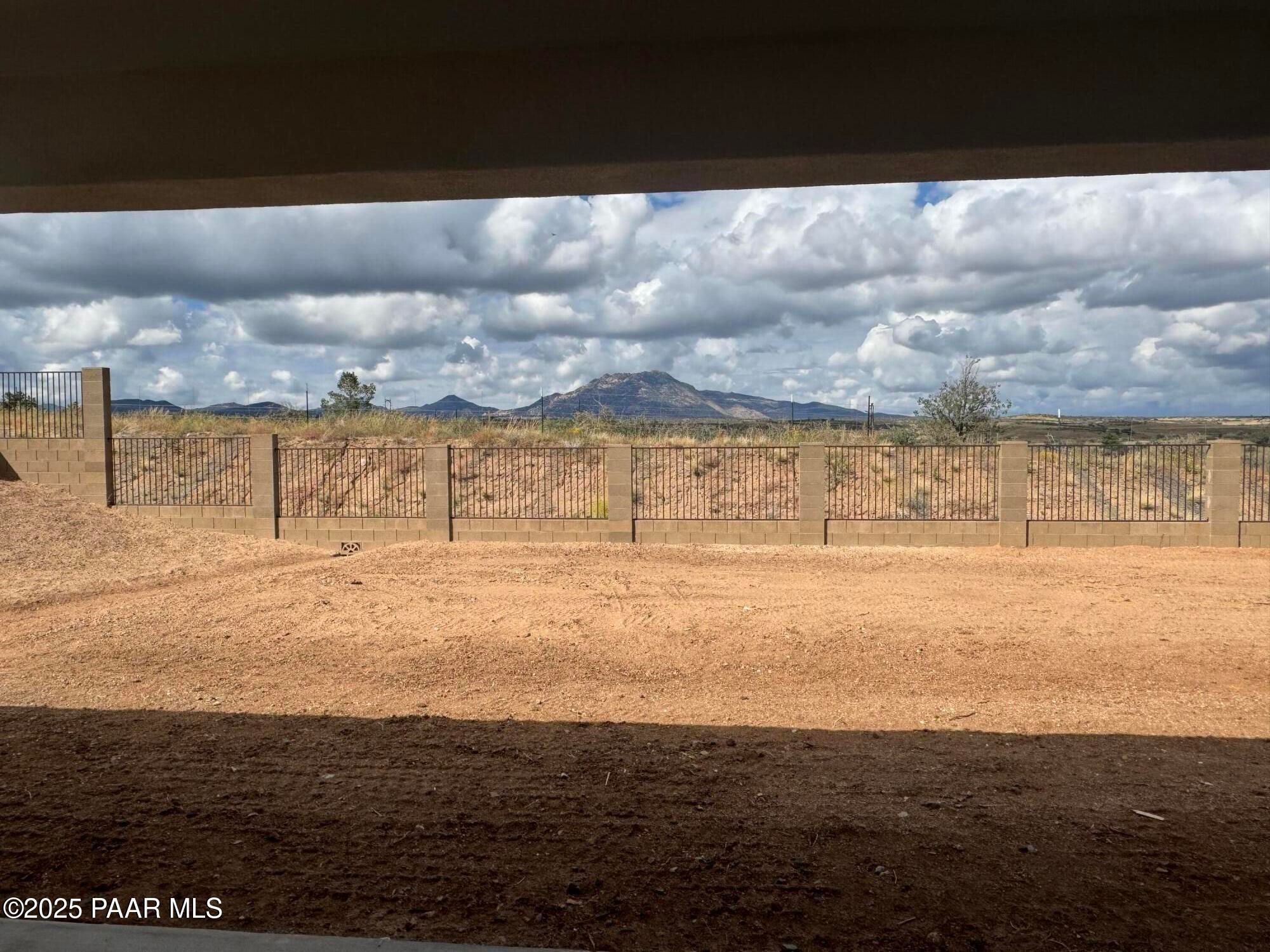 Covered back patio with wrought-iron fence overlooking desert yard and distant mountains under cloudy skies in Prescott, Arizona