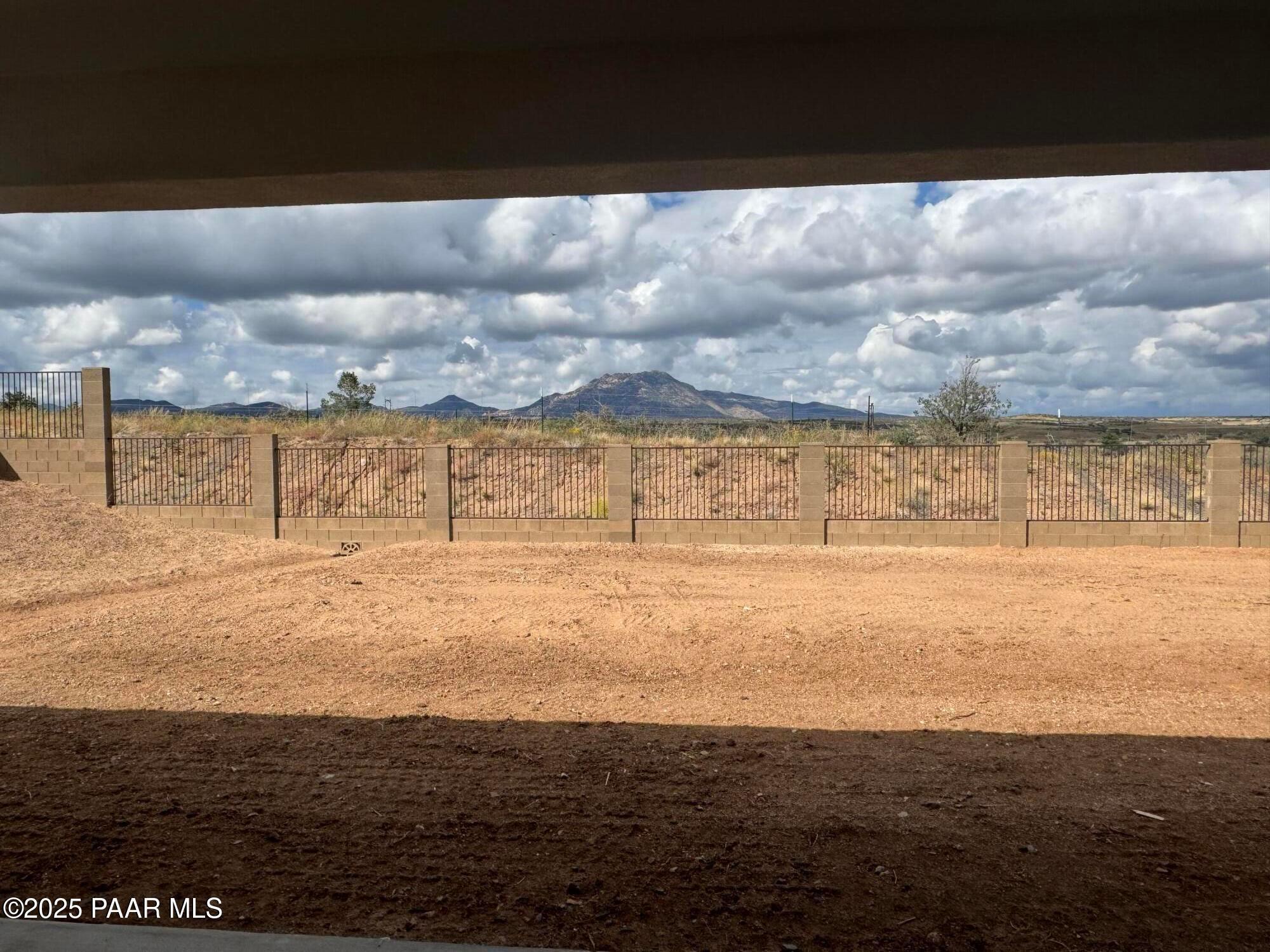 Covered back patio with wrought-iron fence overlooking desert yard and distant mountains under cloudy skies in Prescott, Arizona