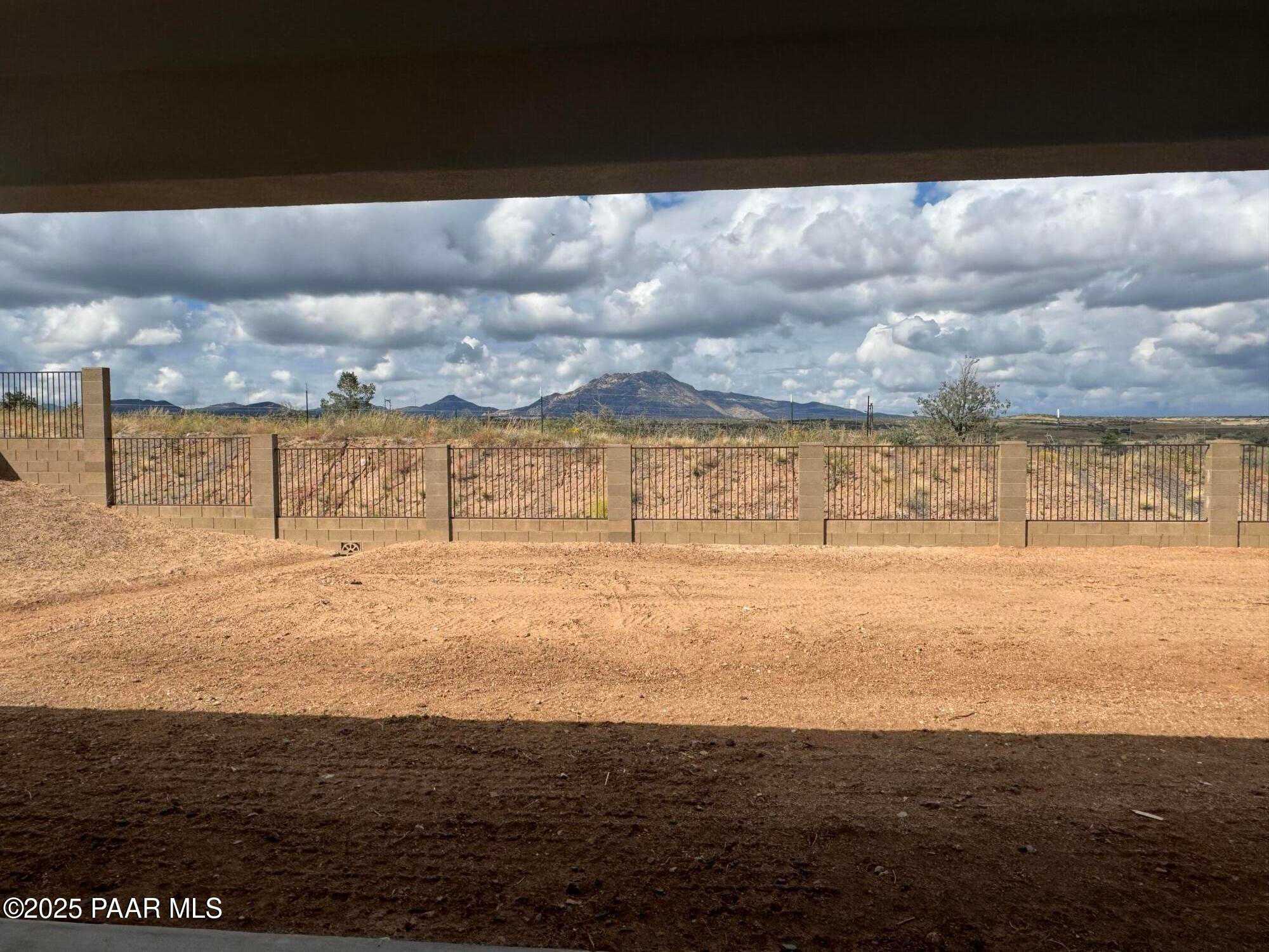 Covered back patio with wrought-iron fence overlooking desert yard and distant mountains under cloudy skies in Prescott, Arizona
