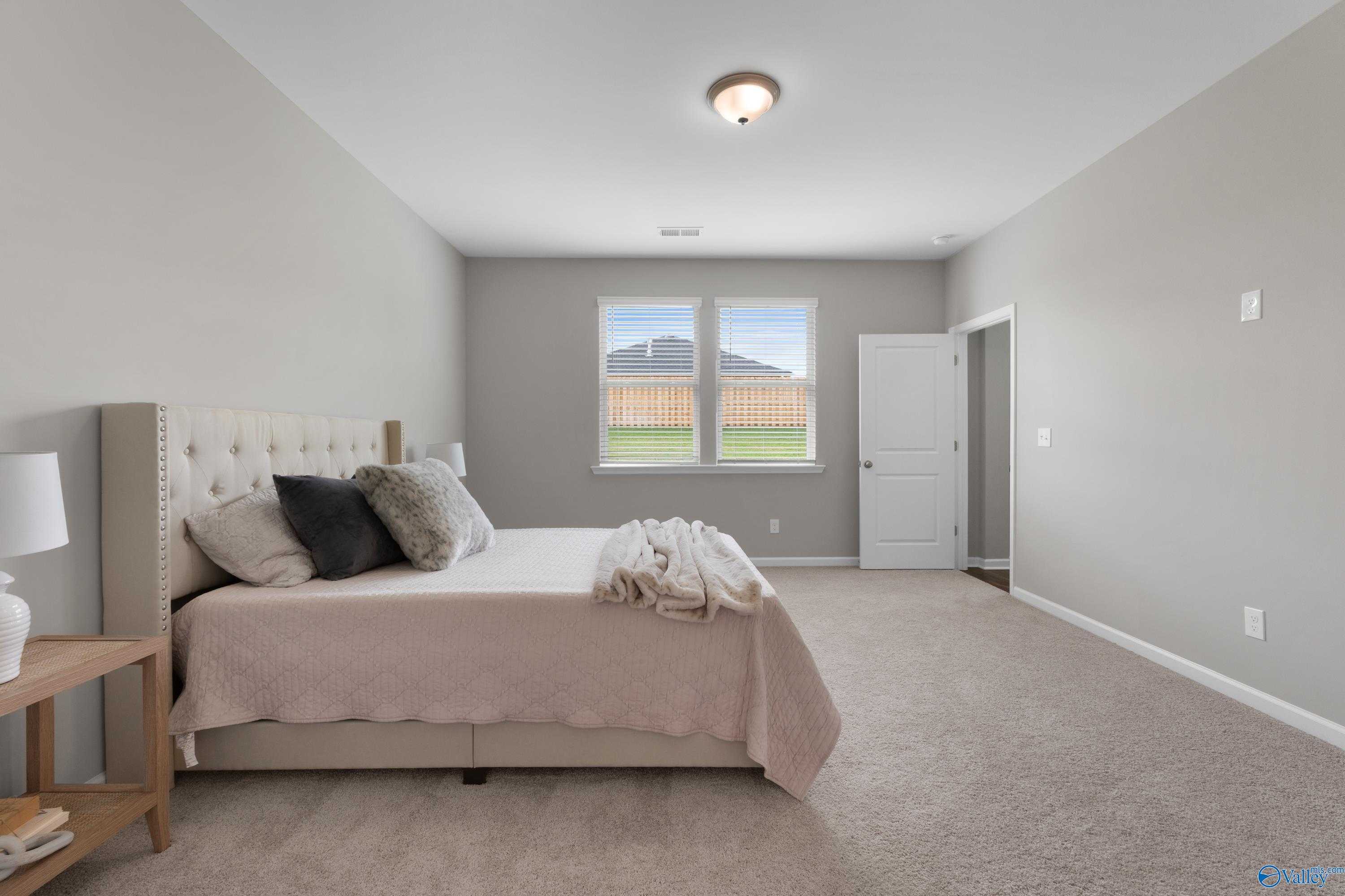 Spacious master bedroom with beige walls, king bed, nightstands, and backyard view in Evermore Homes The Noble, Madison, Alabama