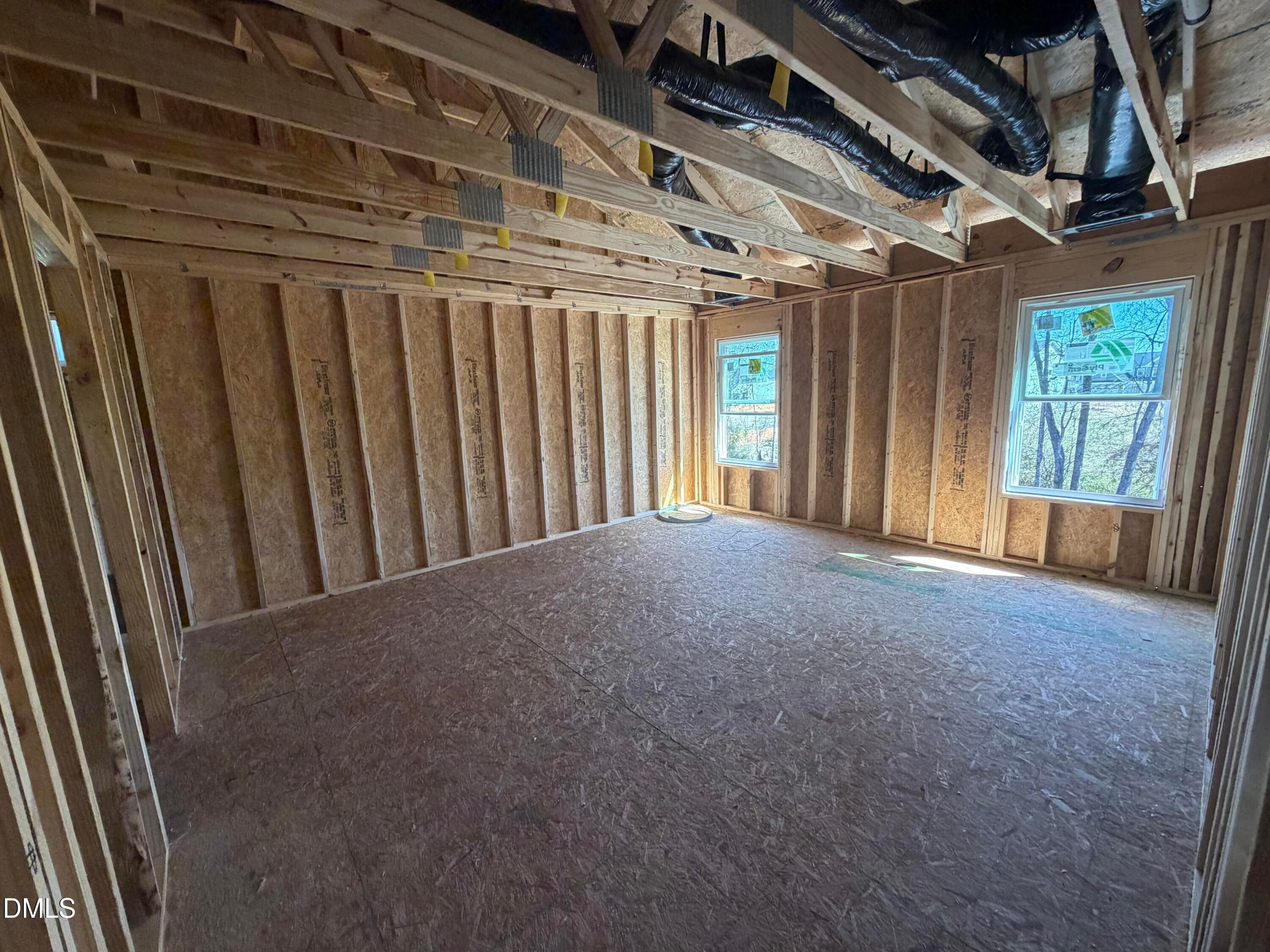 Framed interior room with wooden studs, exposed HVAC ducts, and large windows in The Hickory II B by Davidson Homes, Lillington, NC