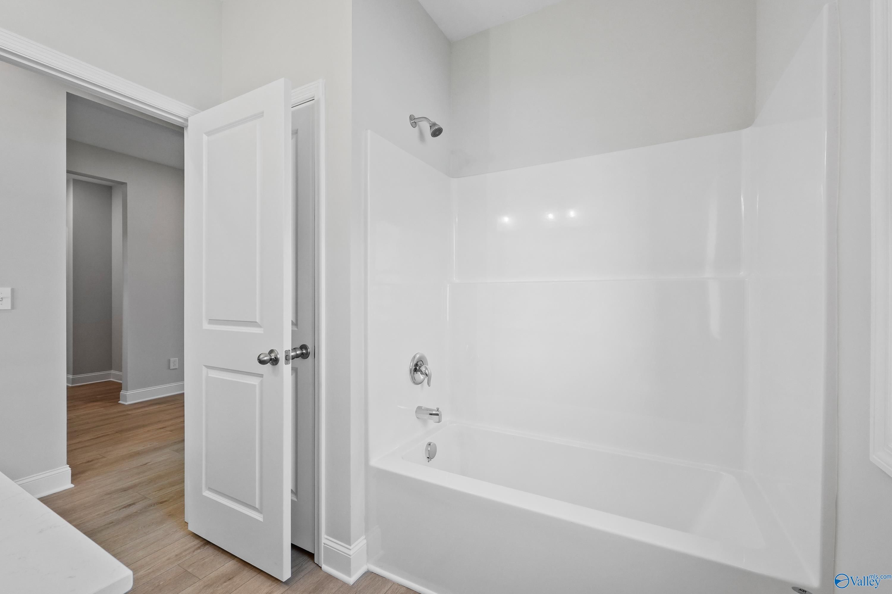 Bright white bathtub and shower combo in modern bathroom with neutral walls and hardwood floors in Davidson Homes The Everett, Hazel Green, AL