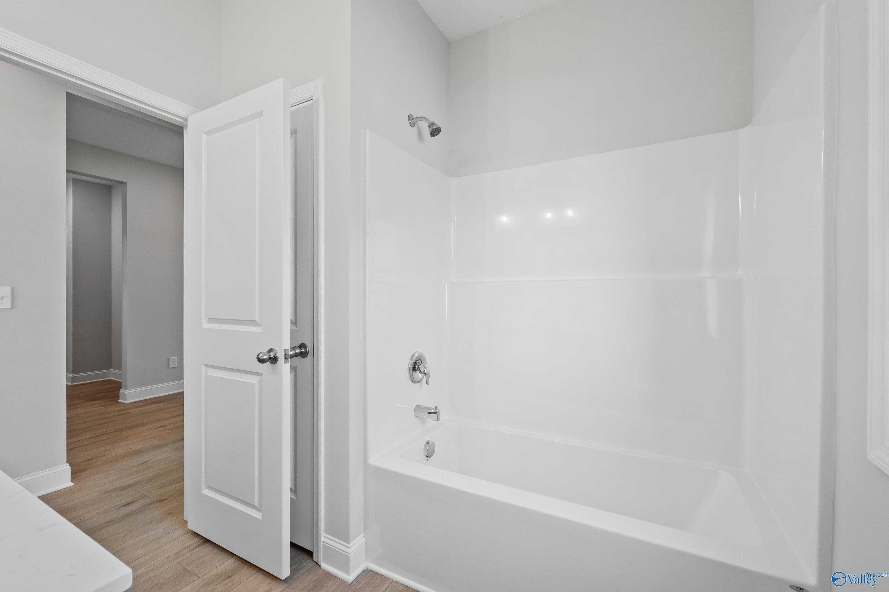 Bright white bathtub and shower combo in modern bathroom with neutral walls and hardwood floors in Davidson Homes The Everett, Hazel Green, AL