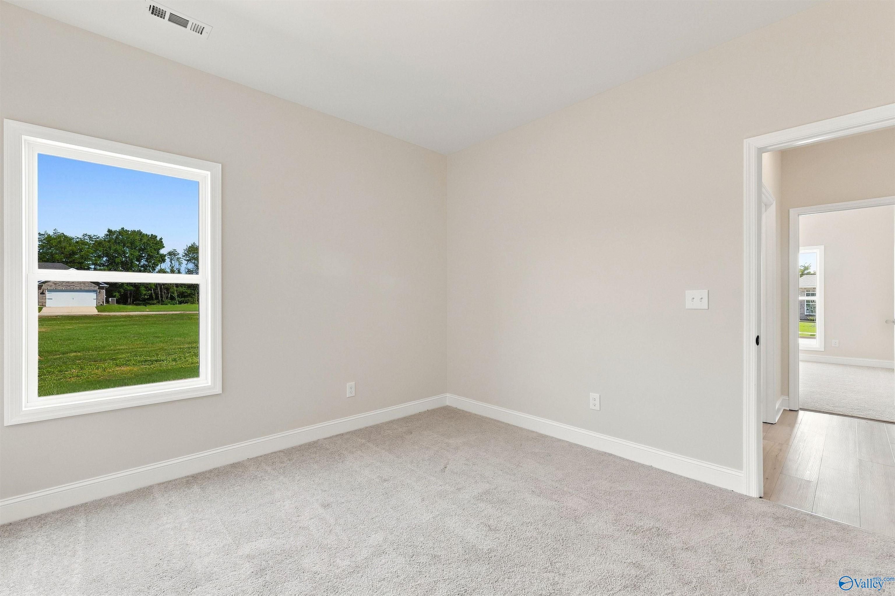 Bright empty bedroom with plush carpet, white trim, and window overlooking green lawn in Davidson Homes The Everett B, Toney, Alabama