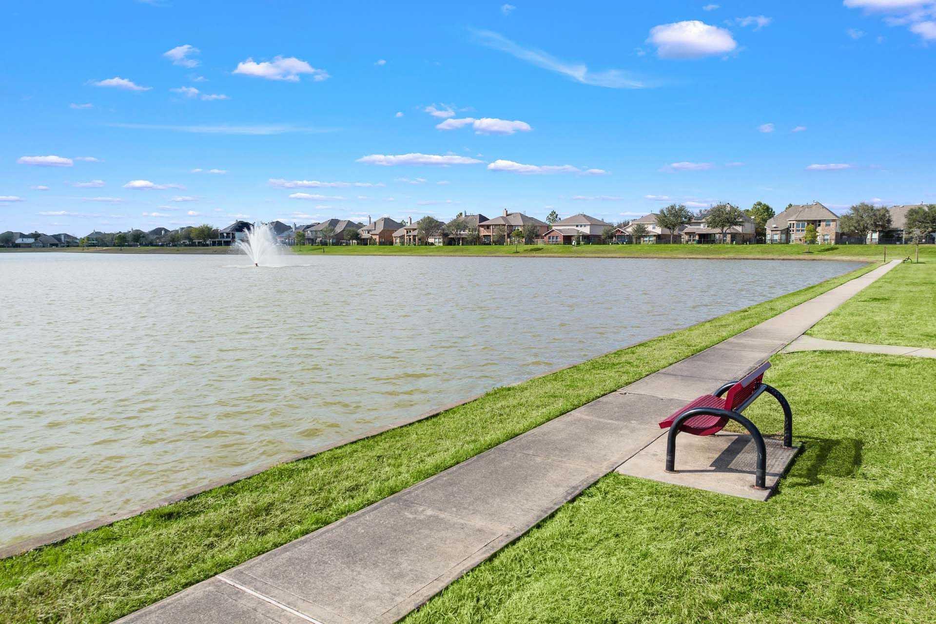 Tranquil lake with fountain, walking path, and red bench at Sierra Vista in Rosharon Texas