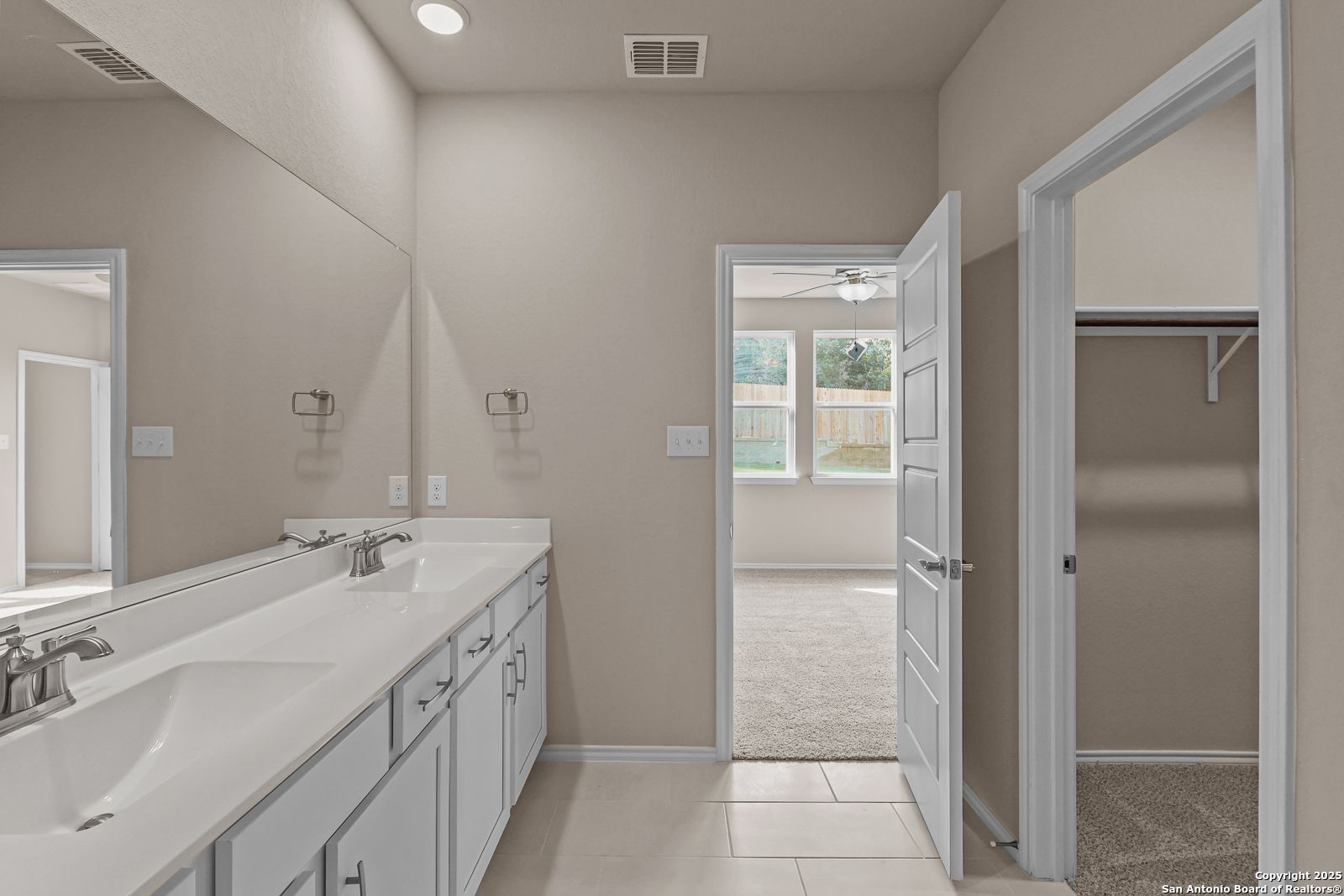 Modern master bathroom featuring double sink vanity, large mirror, and adjacent walk-in closet in Davidson Homes The Douglas G, San Antonio