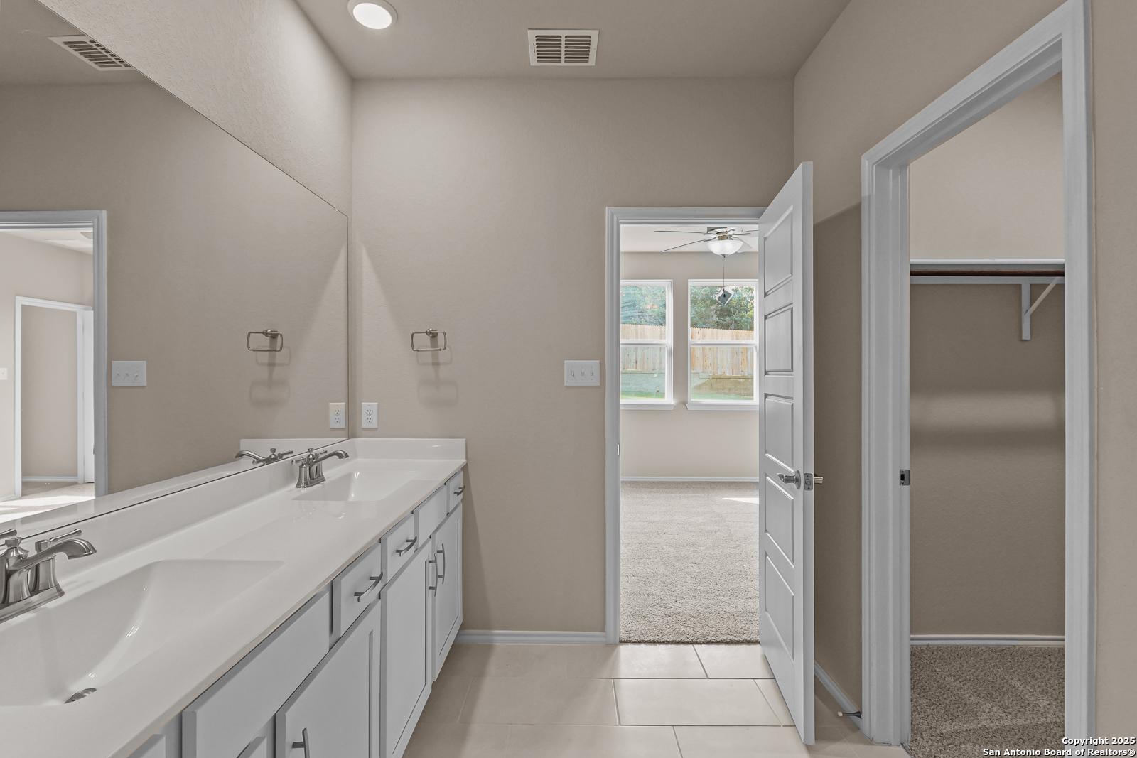 Modern master bathroom featuring double sink vanity, large mirror, and adjacent walk-in closet in Davidson Homes The Douglas G, San Antonio